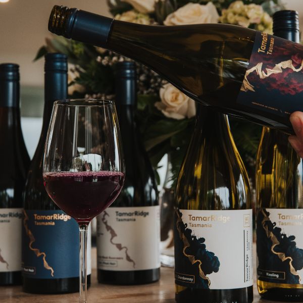 A glass of wine being poured with few bottles in the background