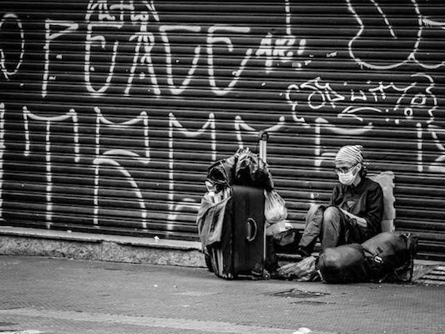 Migrante sentado en la vereda con mochilas pesadas