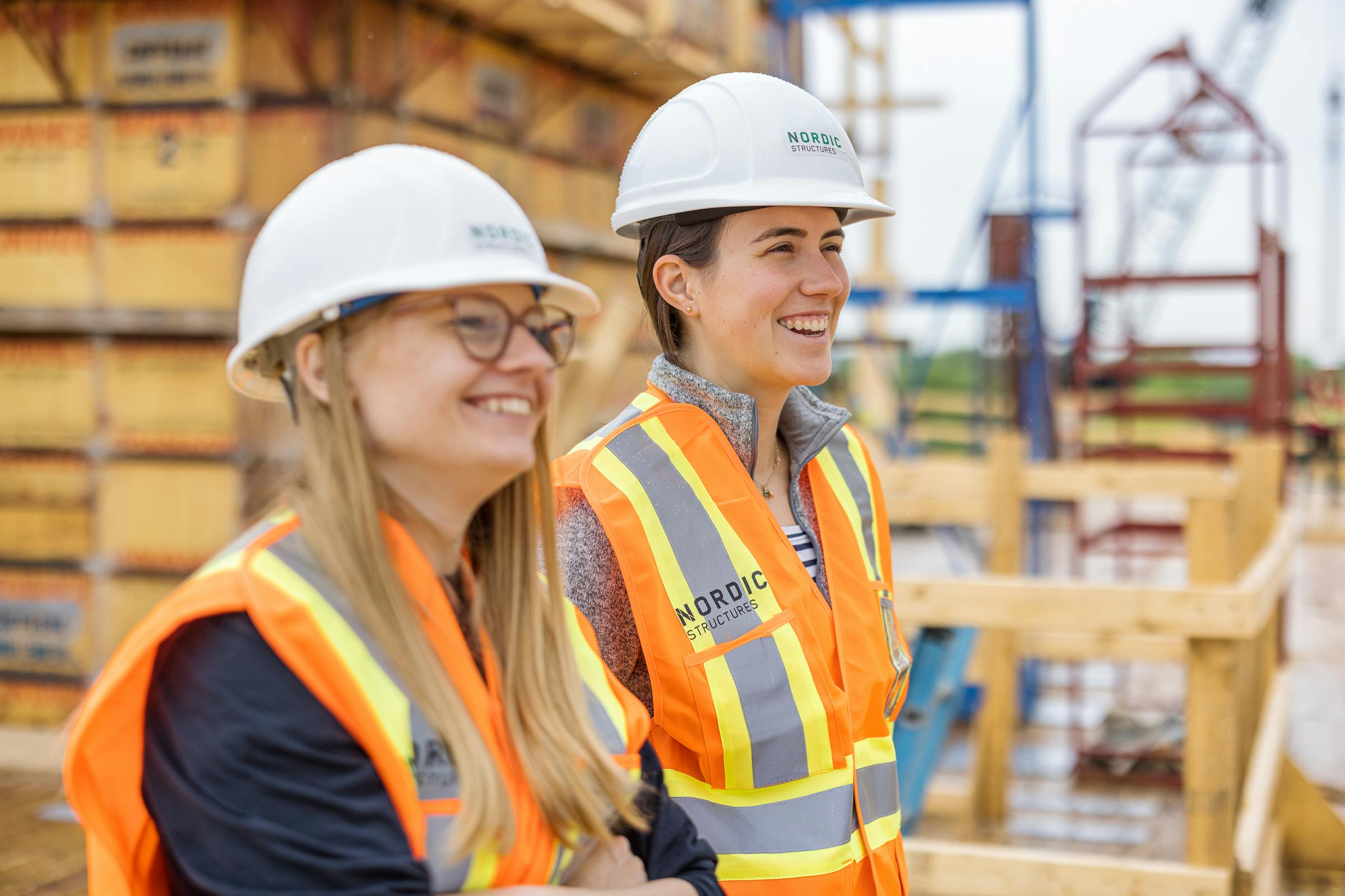 2 female engineers, smiling, on a construction site.