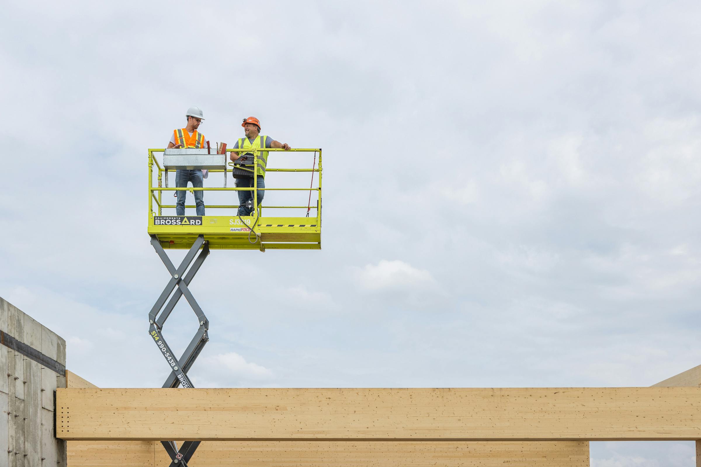 2 workers on a basket overlooking a solid wood structure.