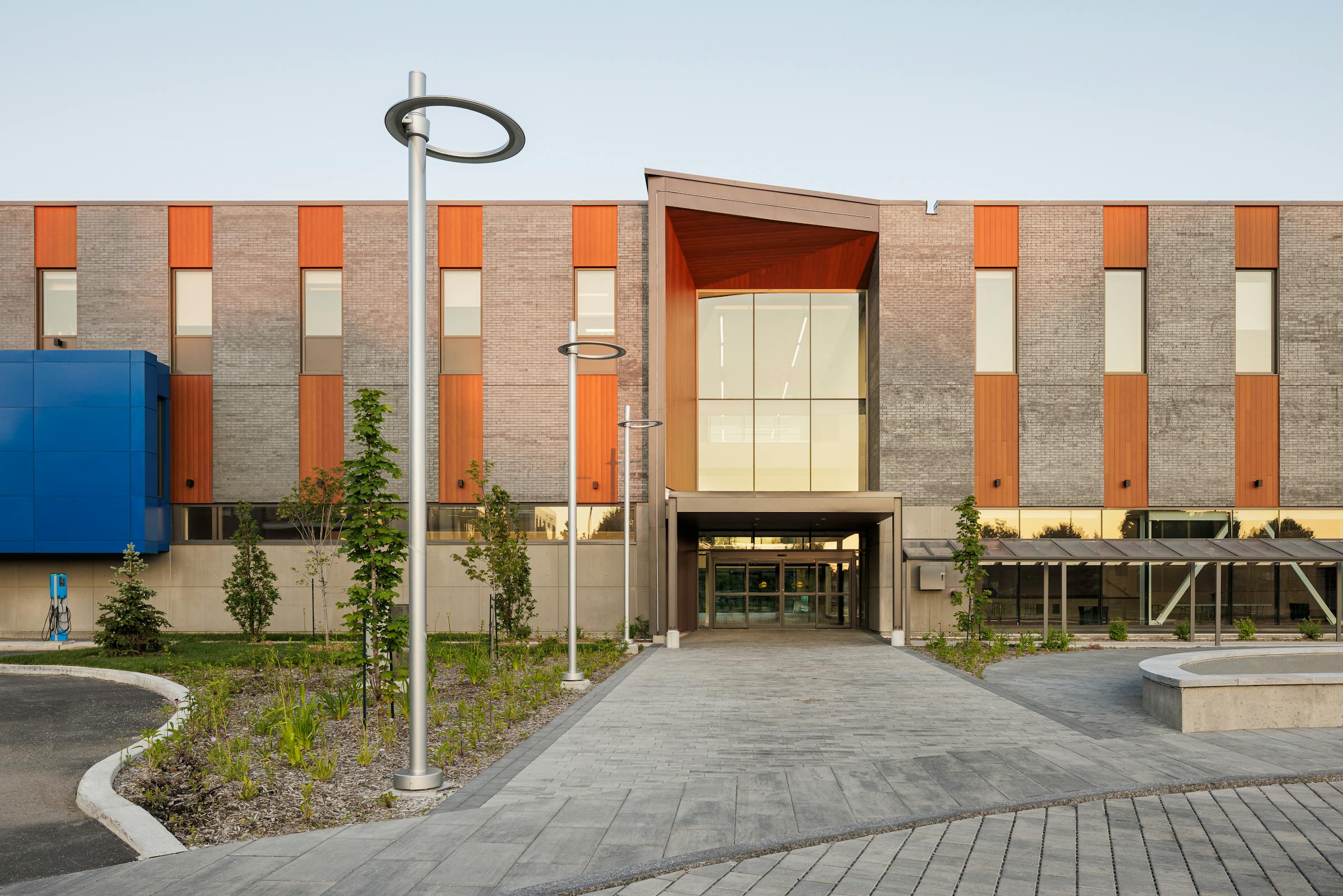 Photographie d'architecture d'un bâtiment institutionnel vu de fasse au lever du soleil. On voit également des lampadaires design et les aménagement paysagé autour de l'entrée.