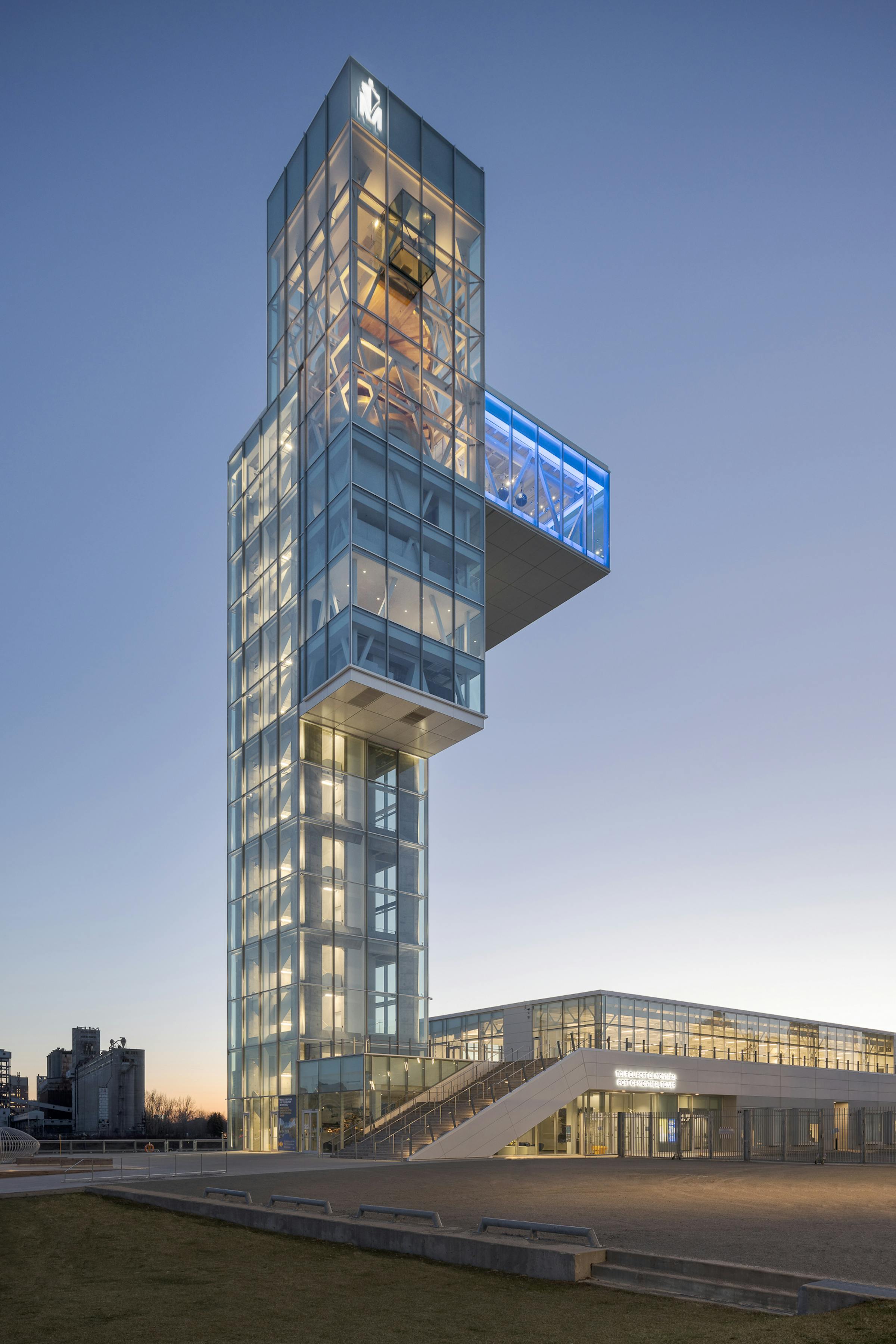 Low-angle view, at nightfall, of a glass tower with a spectacular overhang.