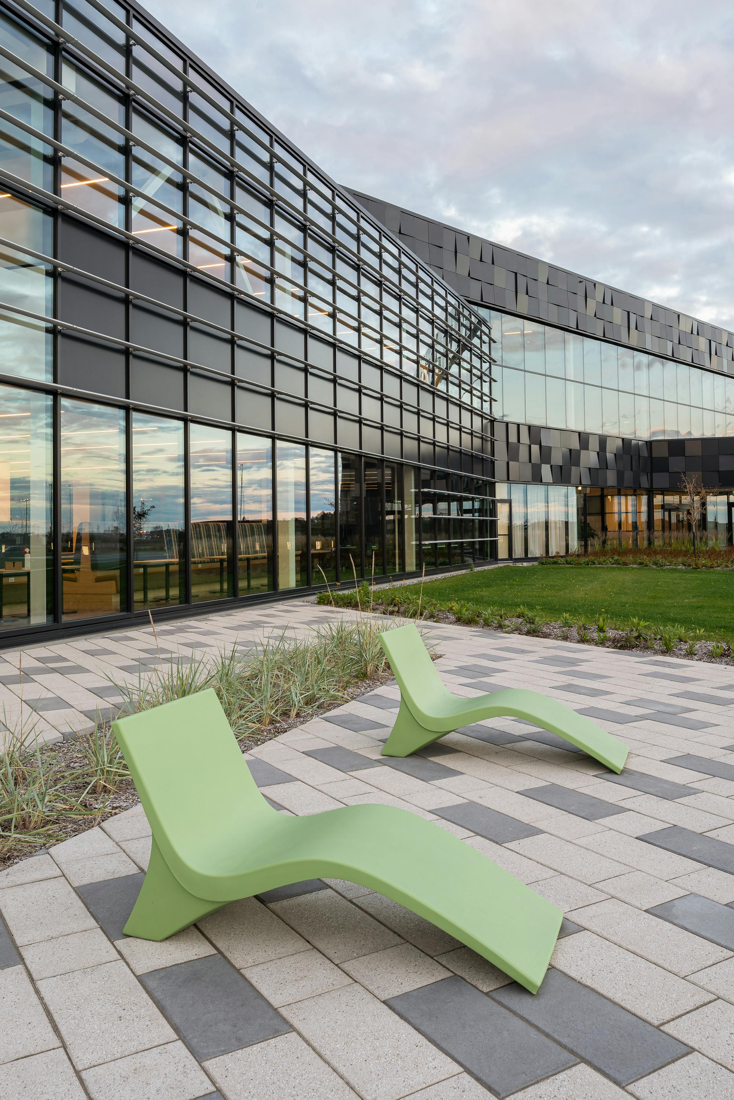 Green deck chairs in front of a building whose windows reflect the sunset.