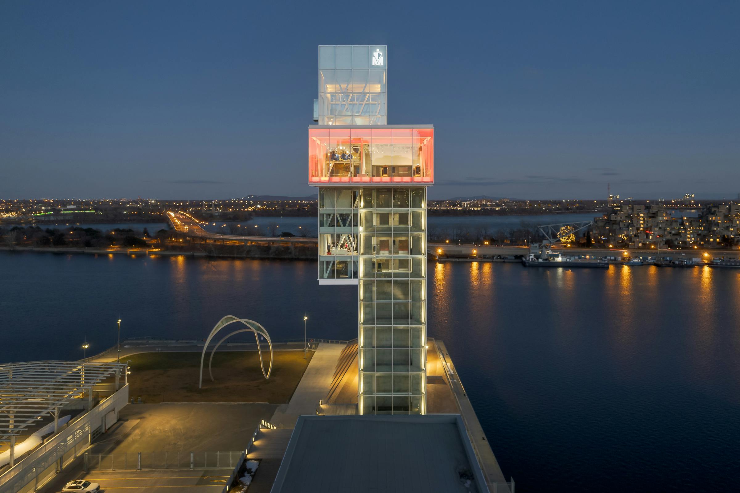 Nighttime aerial architectural photography of the Grand Quai observation tower. The St. Lawrence River in the background.
