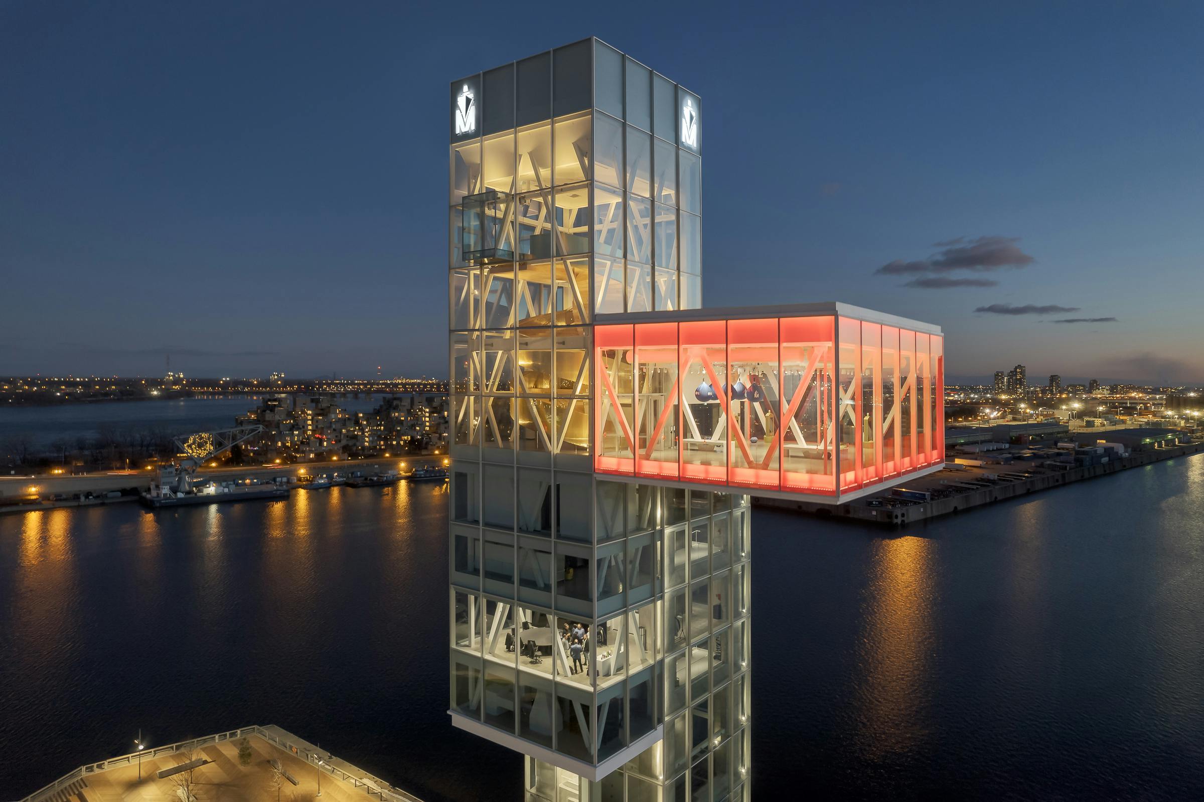 Drone photography of the cantilevered main room of a glass tower. It is dark and the artificial red lighting is dominant.