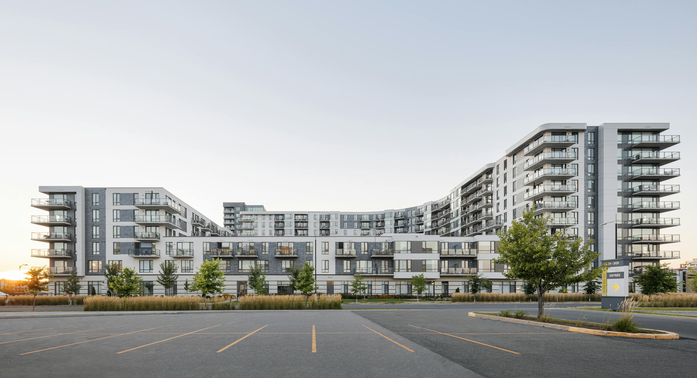 Wide angle photograph of the architecture of a multi-story residence at sunset with a parking lot in the foreground.