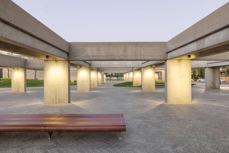 Place publique avec des éléments architecturaux brutalistes et un éclairage publique innovant.