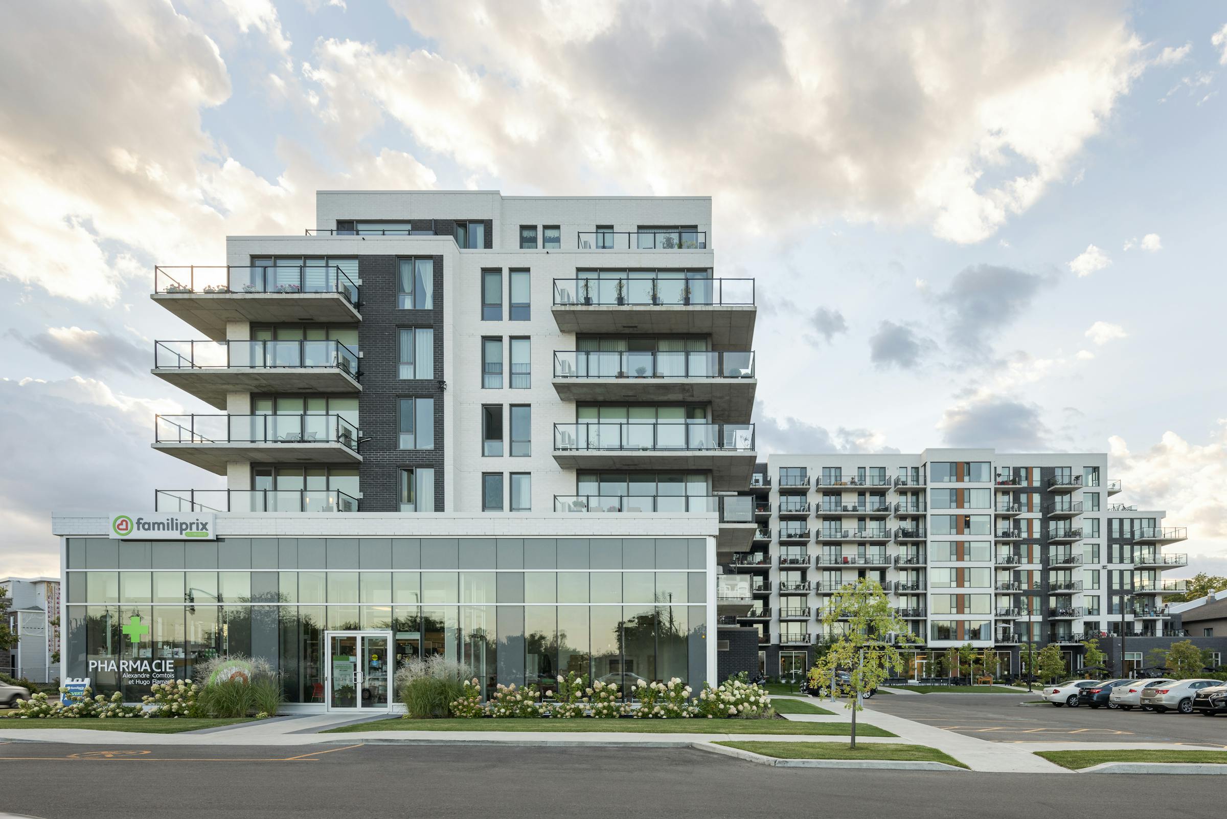 Exterior view of an L-shaped residence with parking and commercial spaces at sunset.