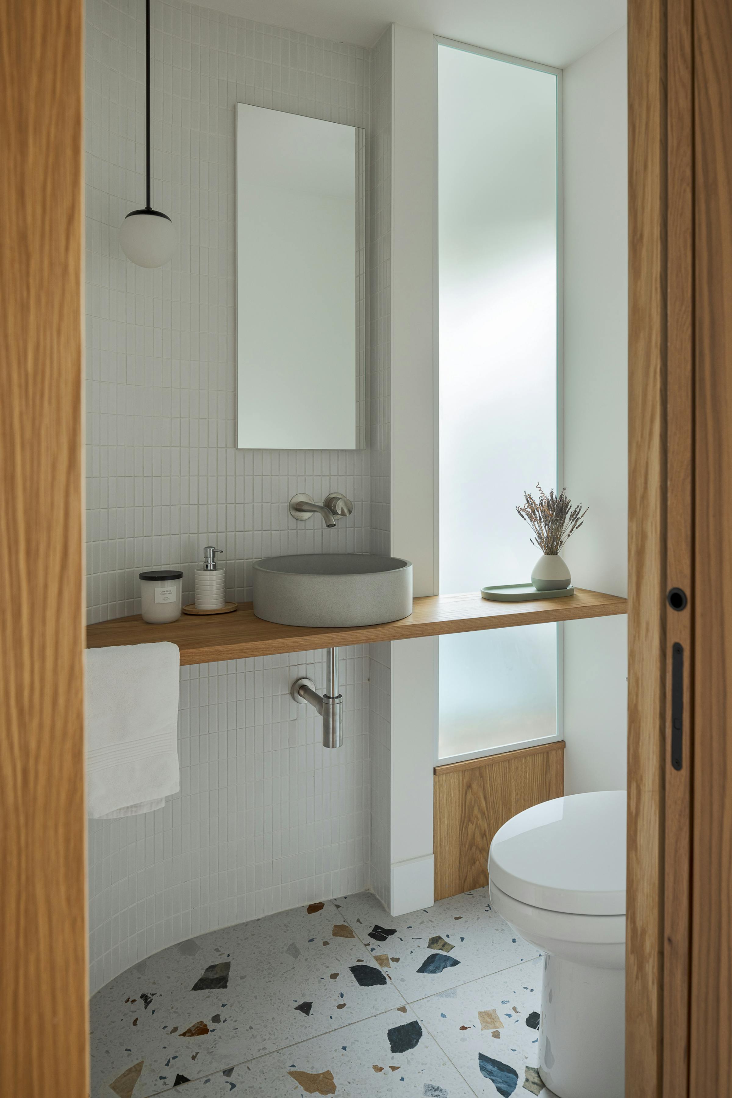 Salle d'eau moderne avec sol en terracotta, bois, murs carrelés et vitre en verre dépoli.