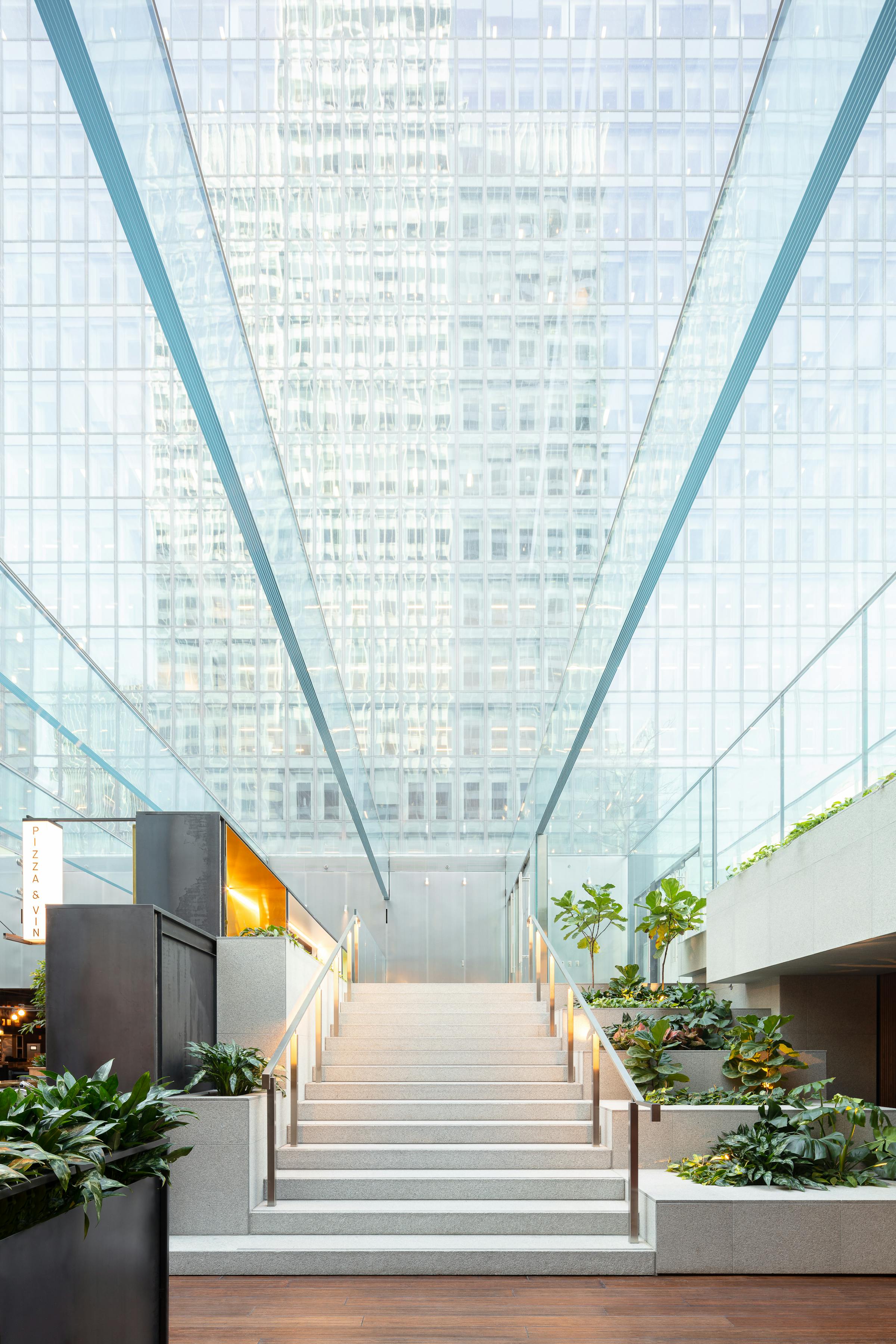 Photograph of the architecture of an interior garden with a glass ceiling. In the background the reflection of Place Ville-Marie on a glass facade