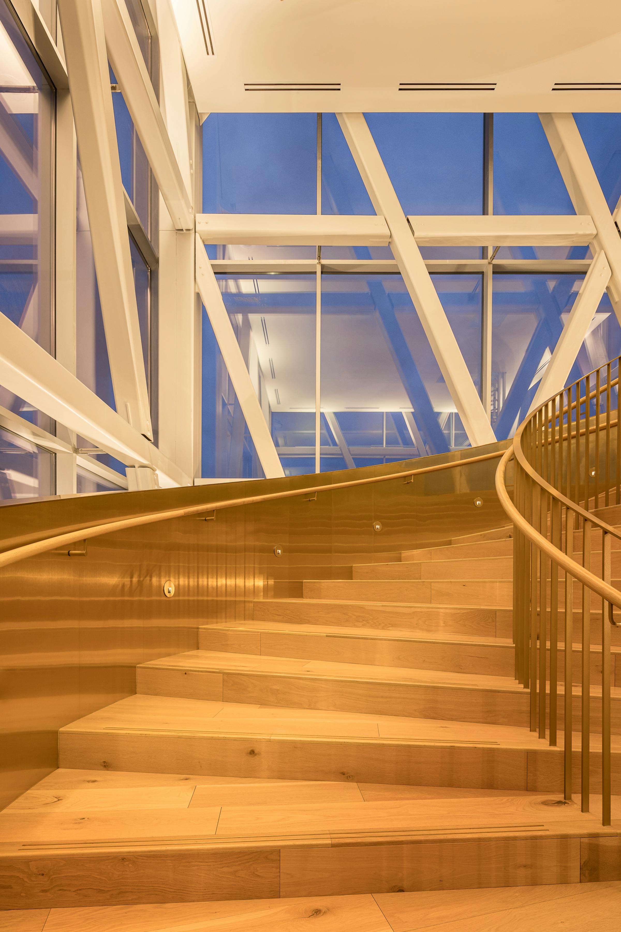 Detail of a wooden spiral staircase in a glass structure.