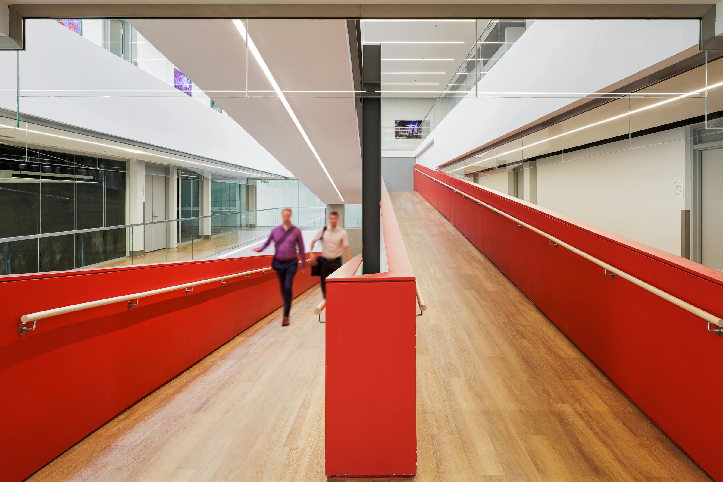 Rampe d'accès universel dans un bâtiment moderne avec des garde du cour rouge et des silhouette en mouvement.
