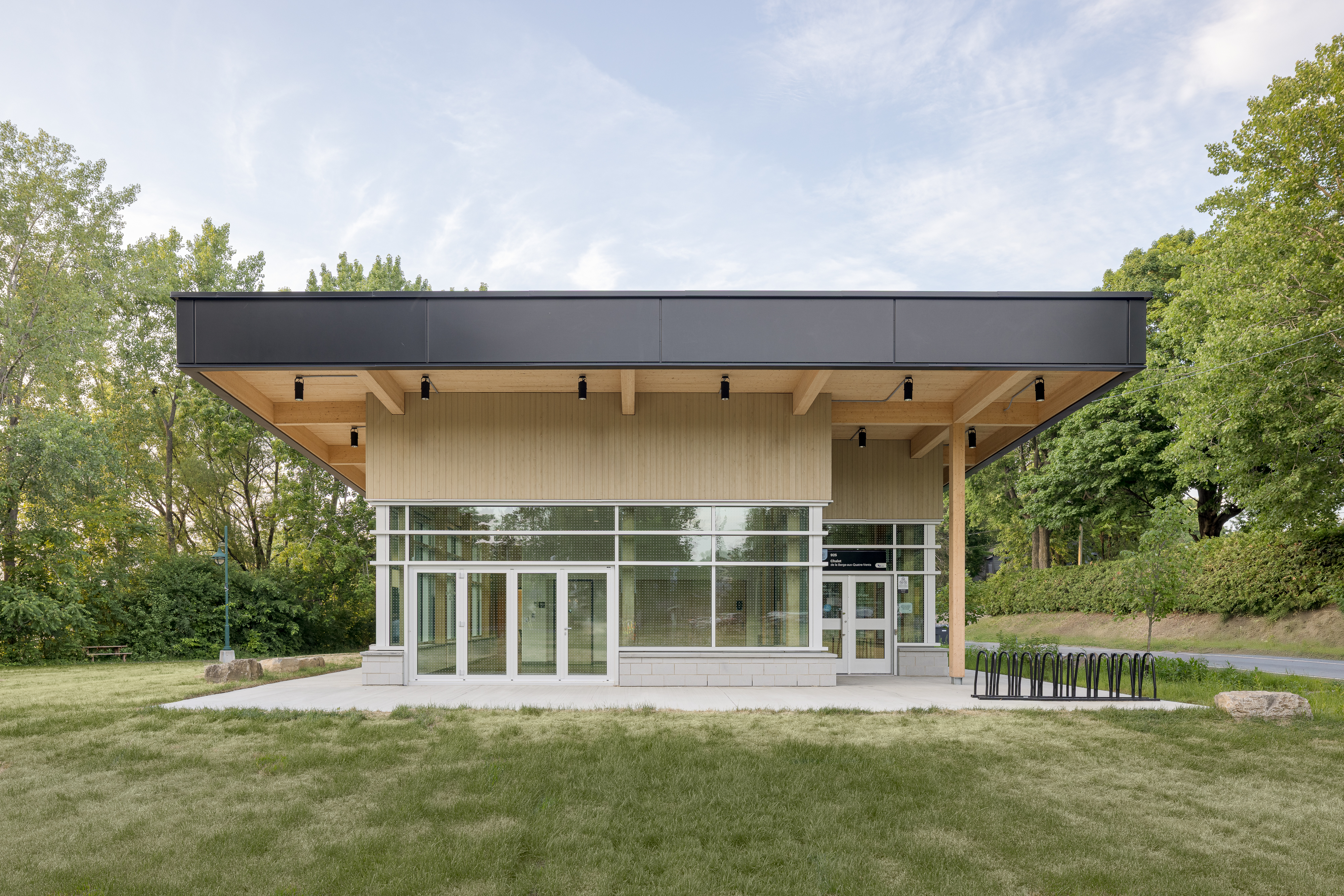 Photographie grand angle du chalet d'accueil vu depuis la pelouse environnante, illustrant l'intégration du bâtiment au site naturel de la berge.