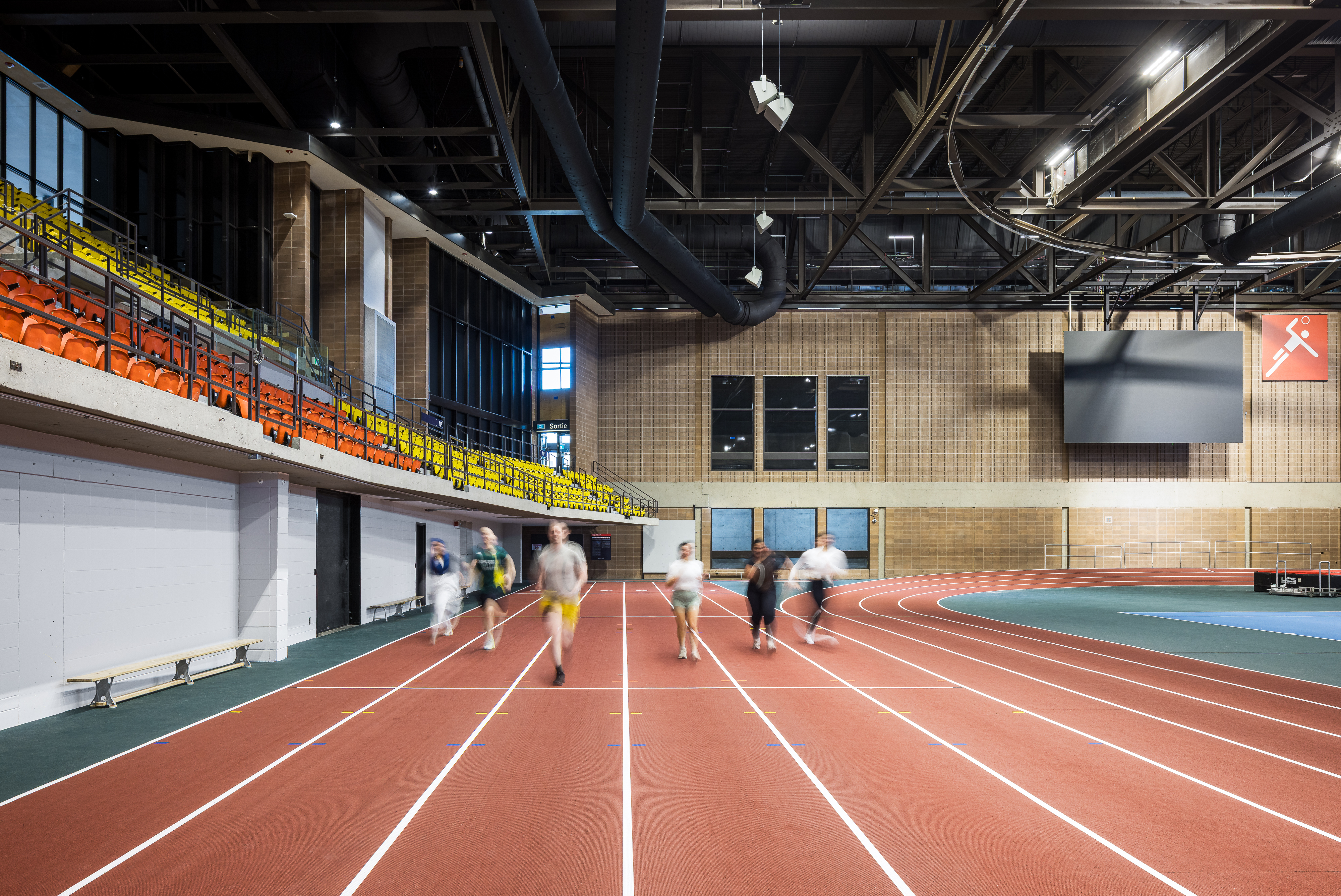 Photograph of institutional building, runners on the athletics track seen from the stands.