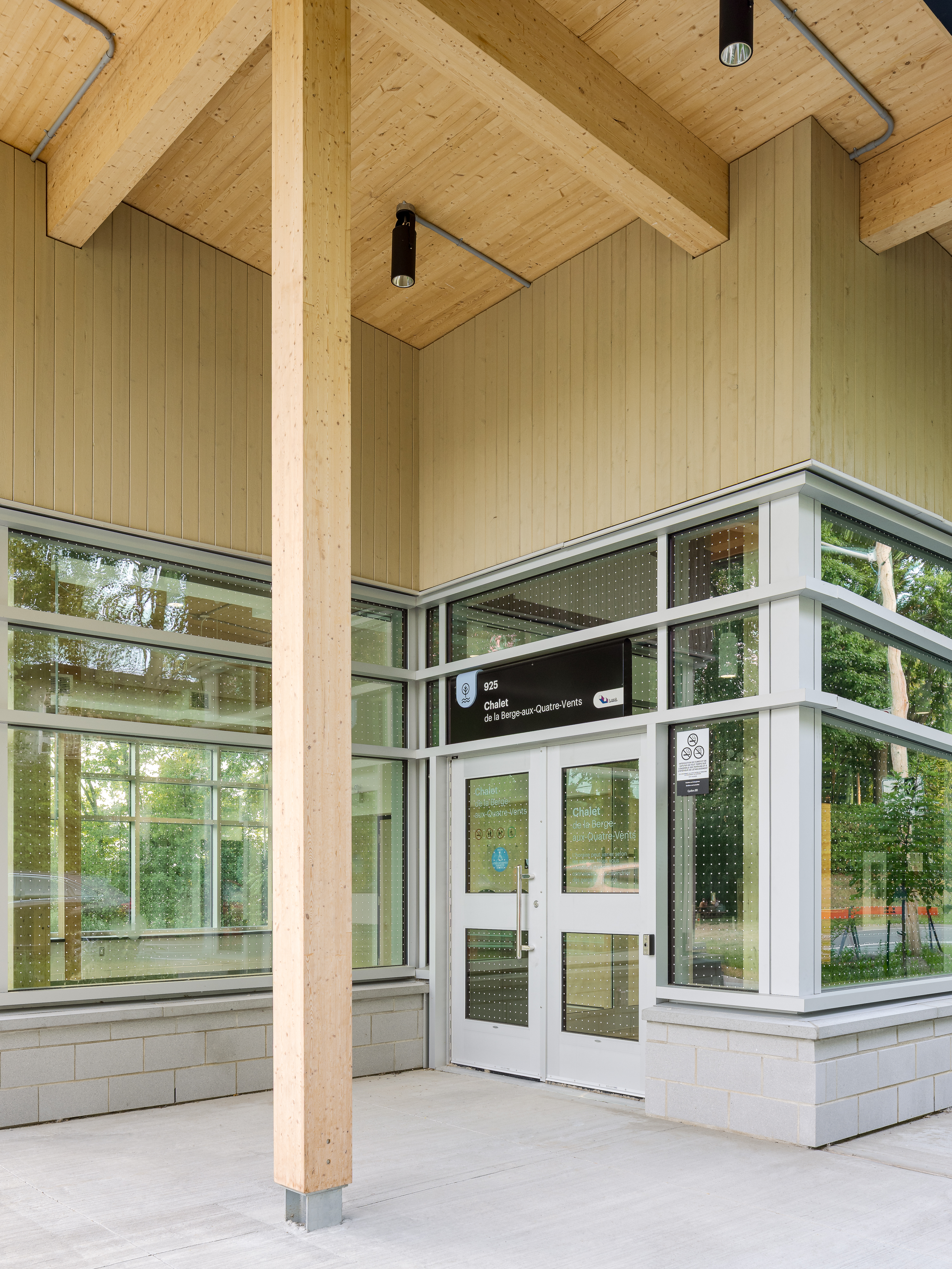 Photographie détaillée de la structure en bois du chalet, avec un poteau porteur et la porte d'entrée vitrée à l'angle du bâtiment.