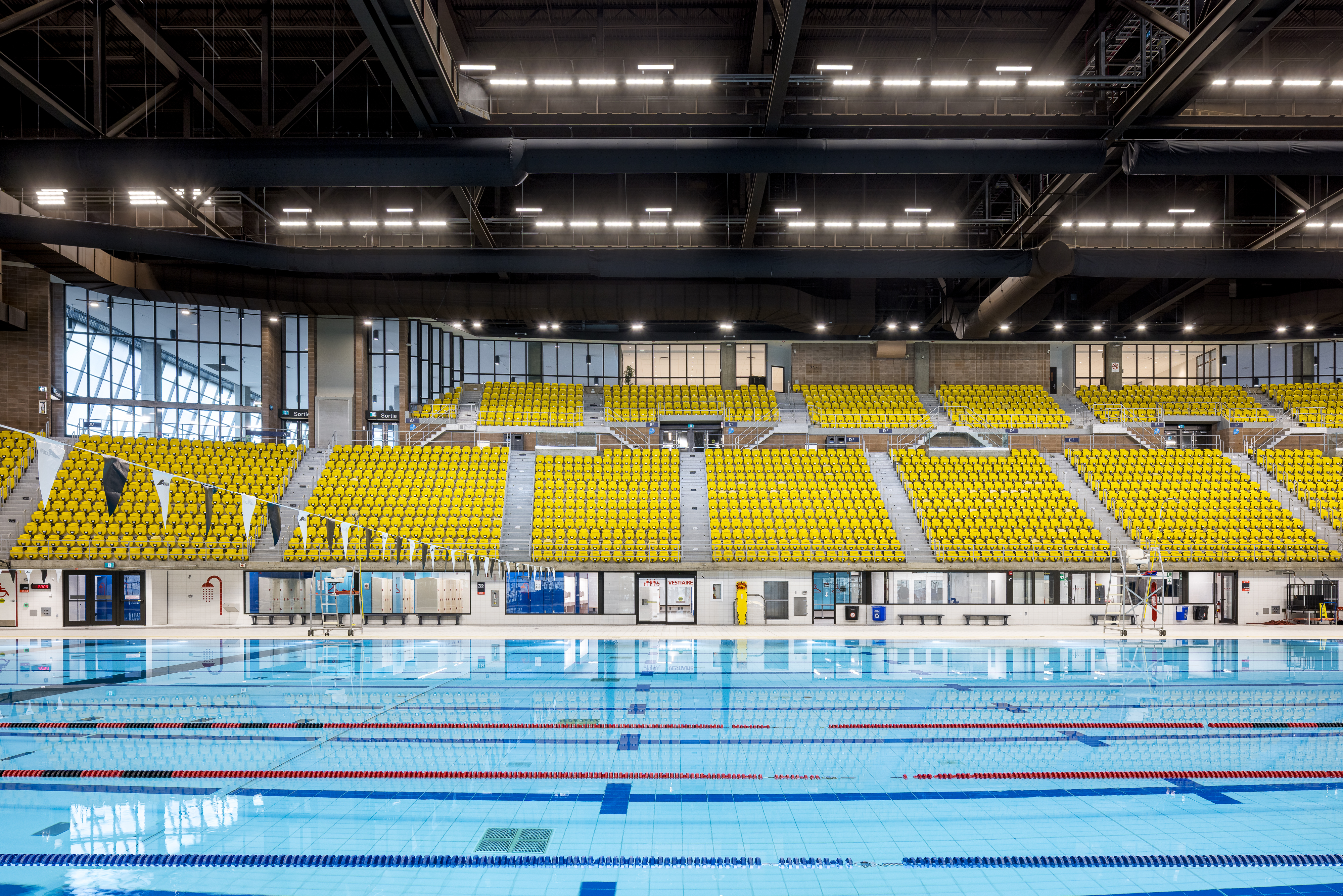 Architectural photograph of the renovated swimming pool, with yellow and orange bleachers in the background.