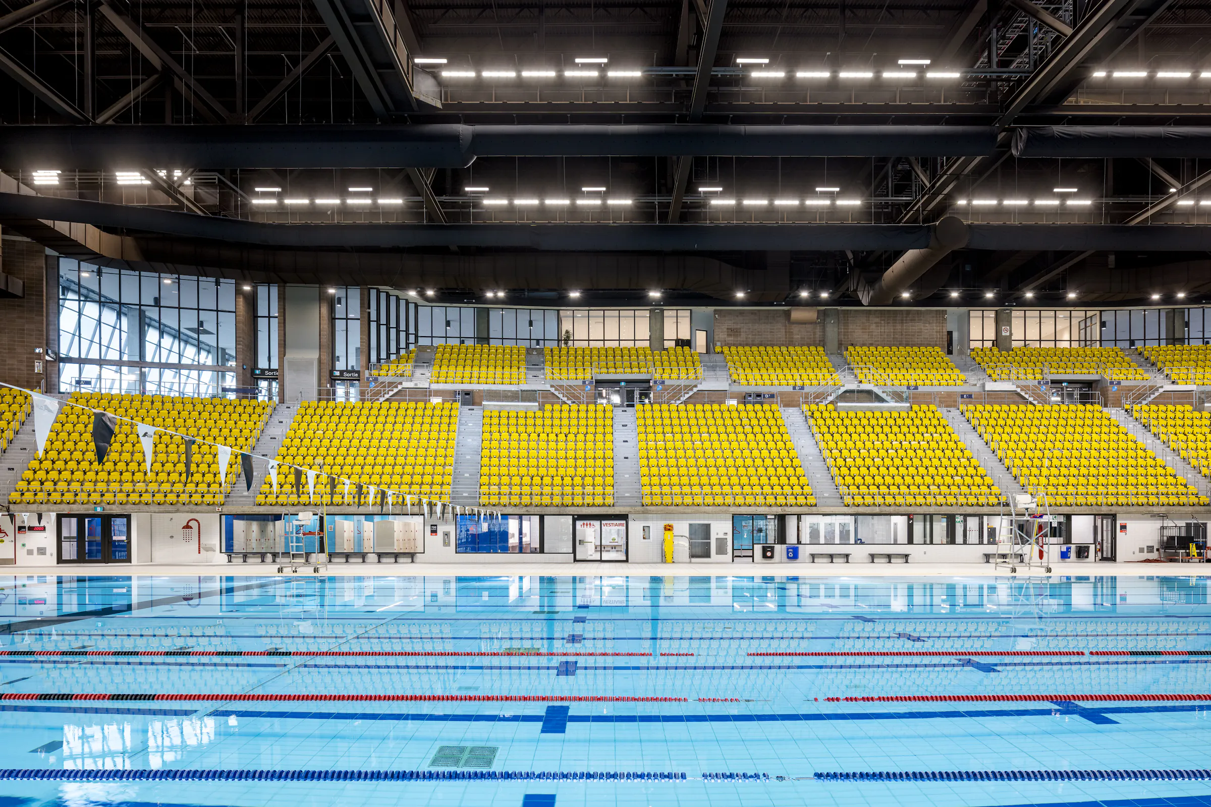 Architectural photograph of the renovated swimming pool, with yellow and orange bleachers in the background.