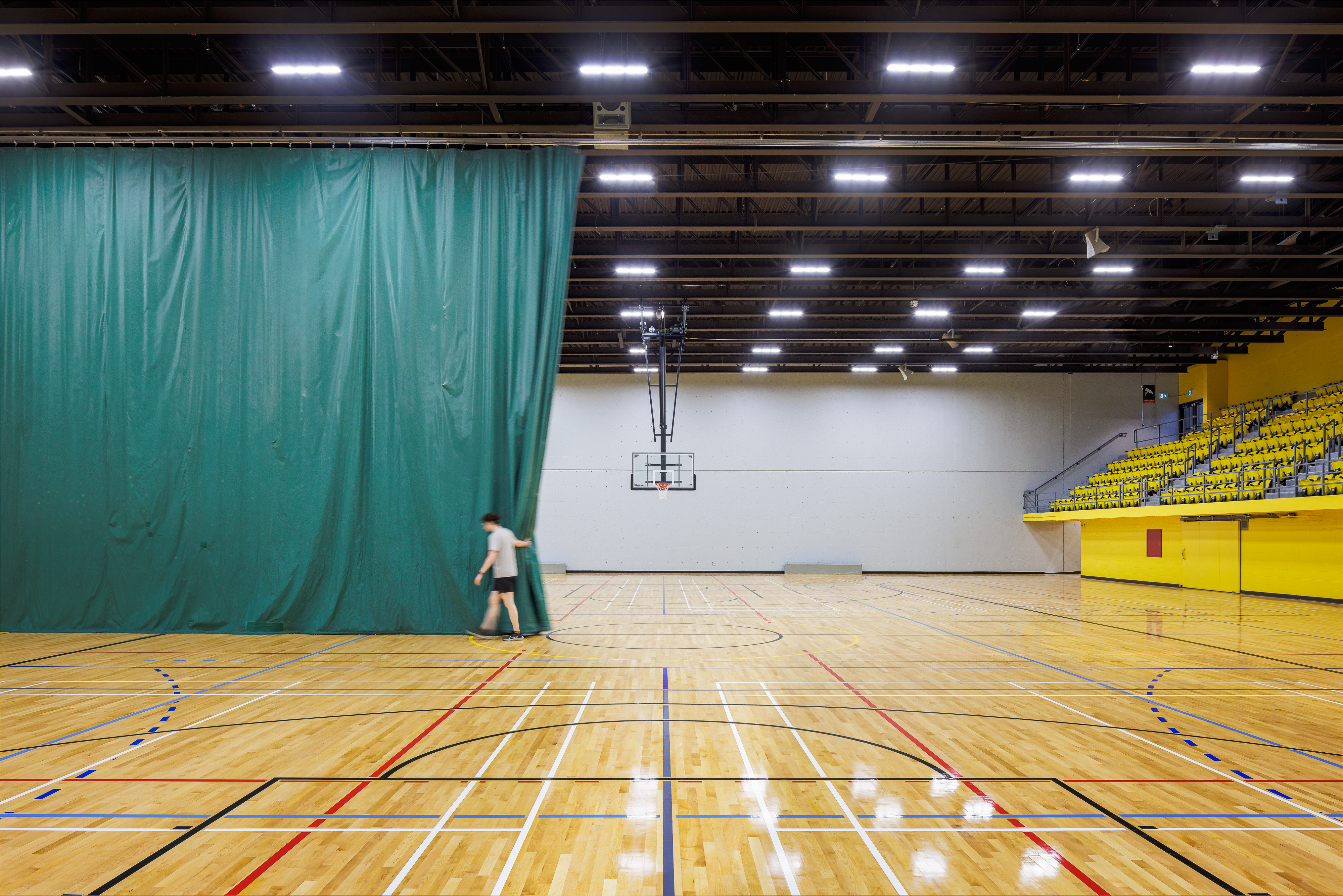 Interior architecture photograph, green partition curtain in the double gymnasium, sports floor and exposed beams.