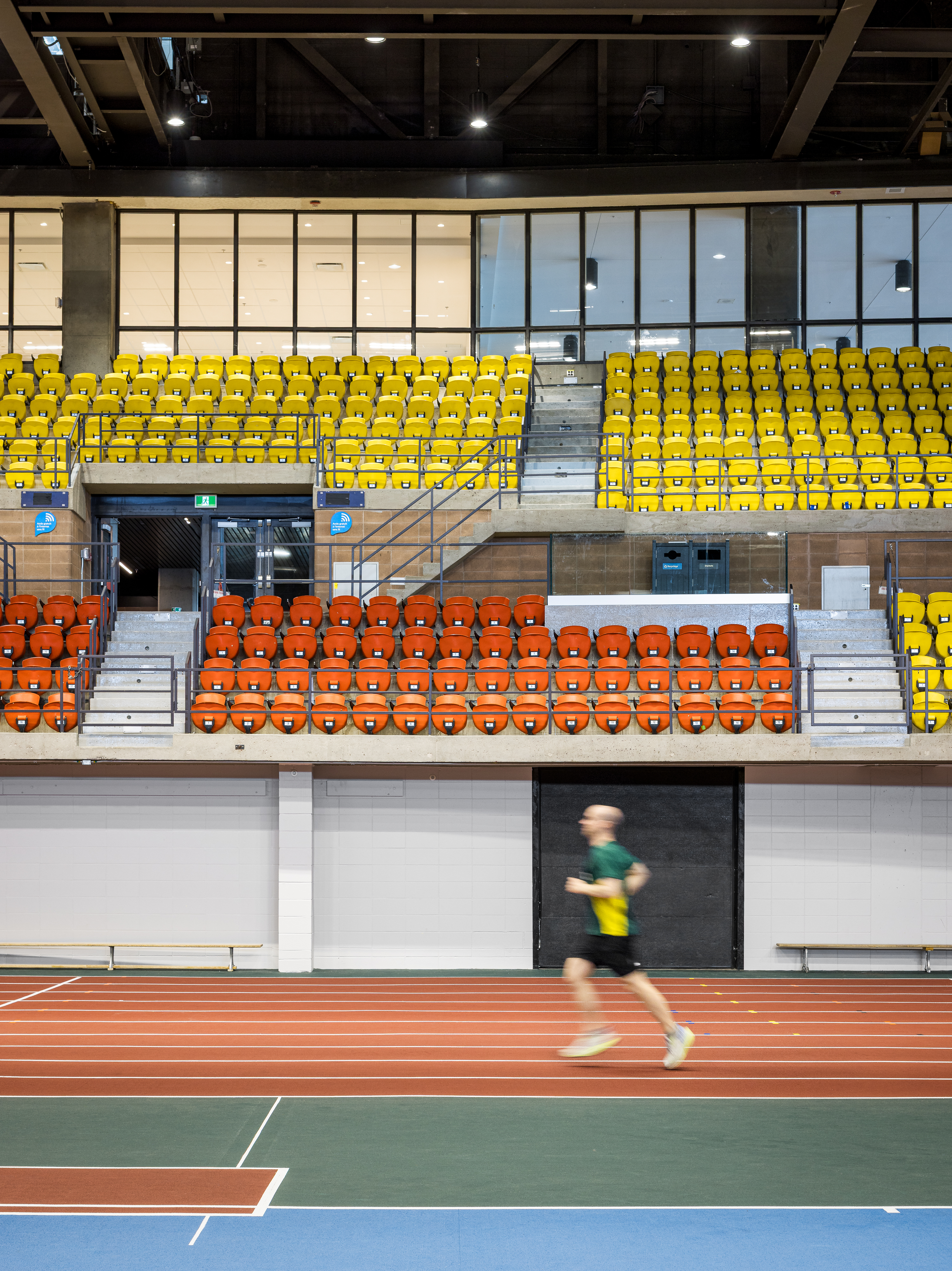 Photograph of industrial architecture, yellow and orange bleachers, exposed steel roof structure.