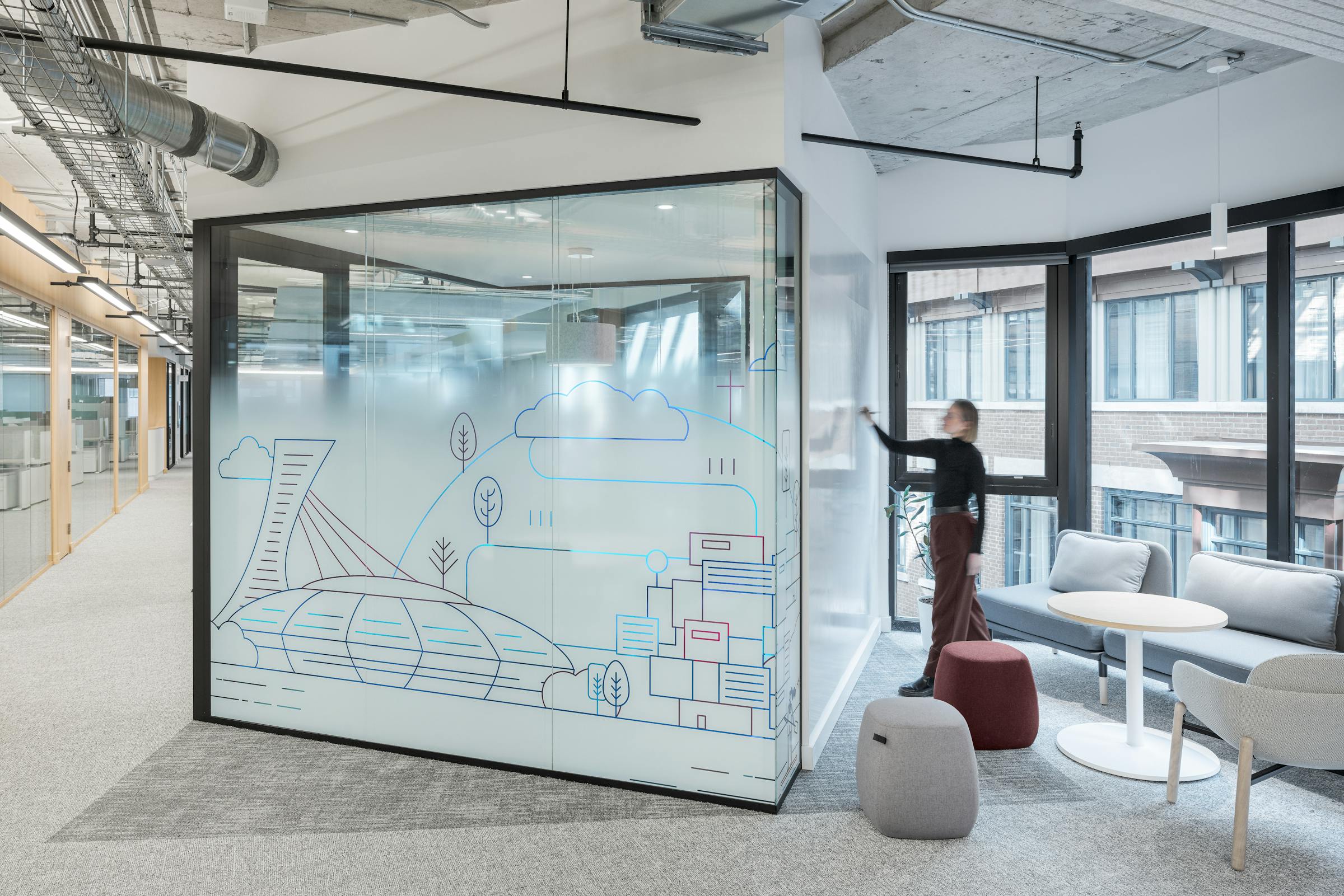 Une employé dessine sur un mur tableau blanc dans un espace de travail ouvert avec des élément de design rappelant la ville de Montréal.