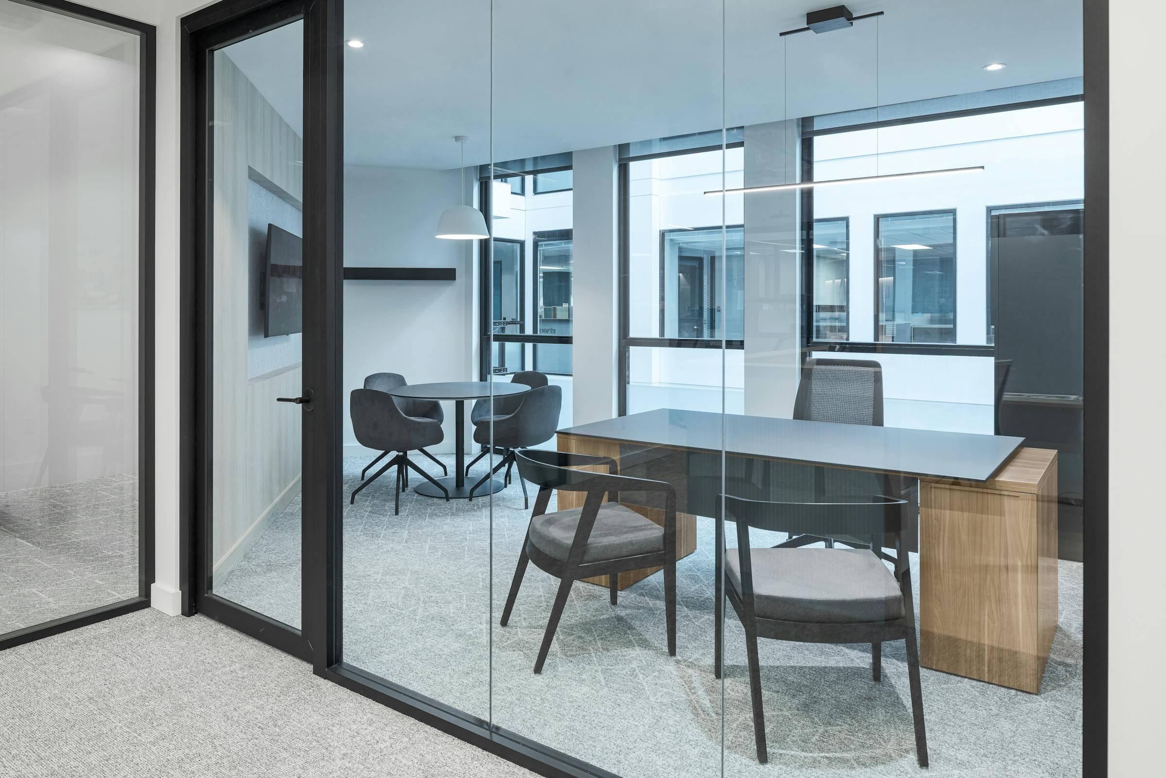 Bureau au design moderne et avec du mobilier ergonomique photographié au travers d'une partie architecturale en verre.