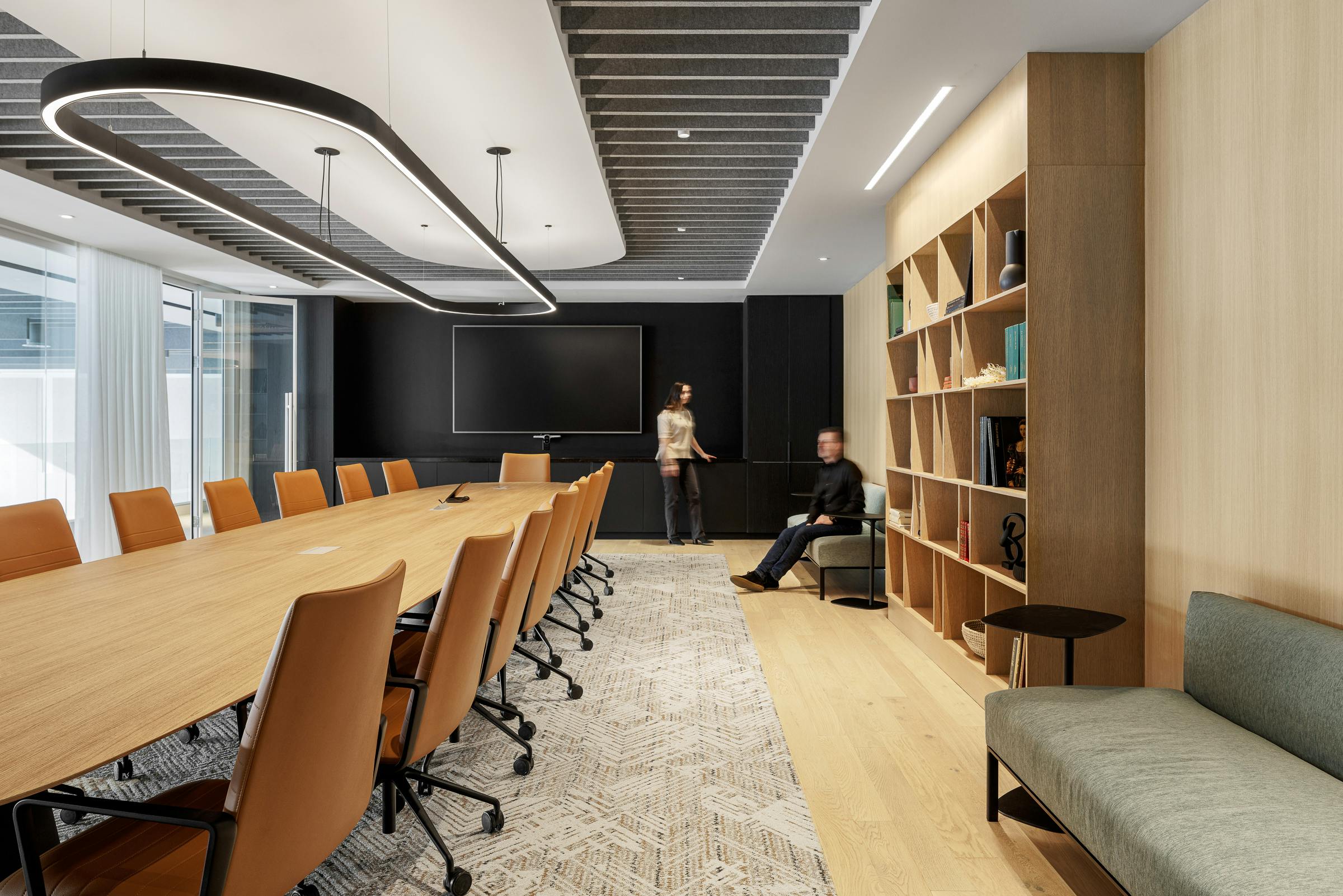 Two silhouettes posing in a meeting room with a long wooden table and a black wall.