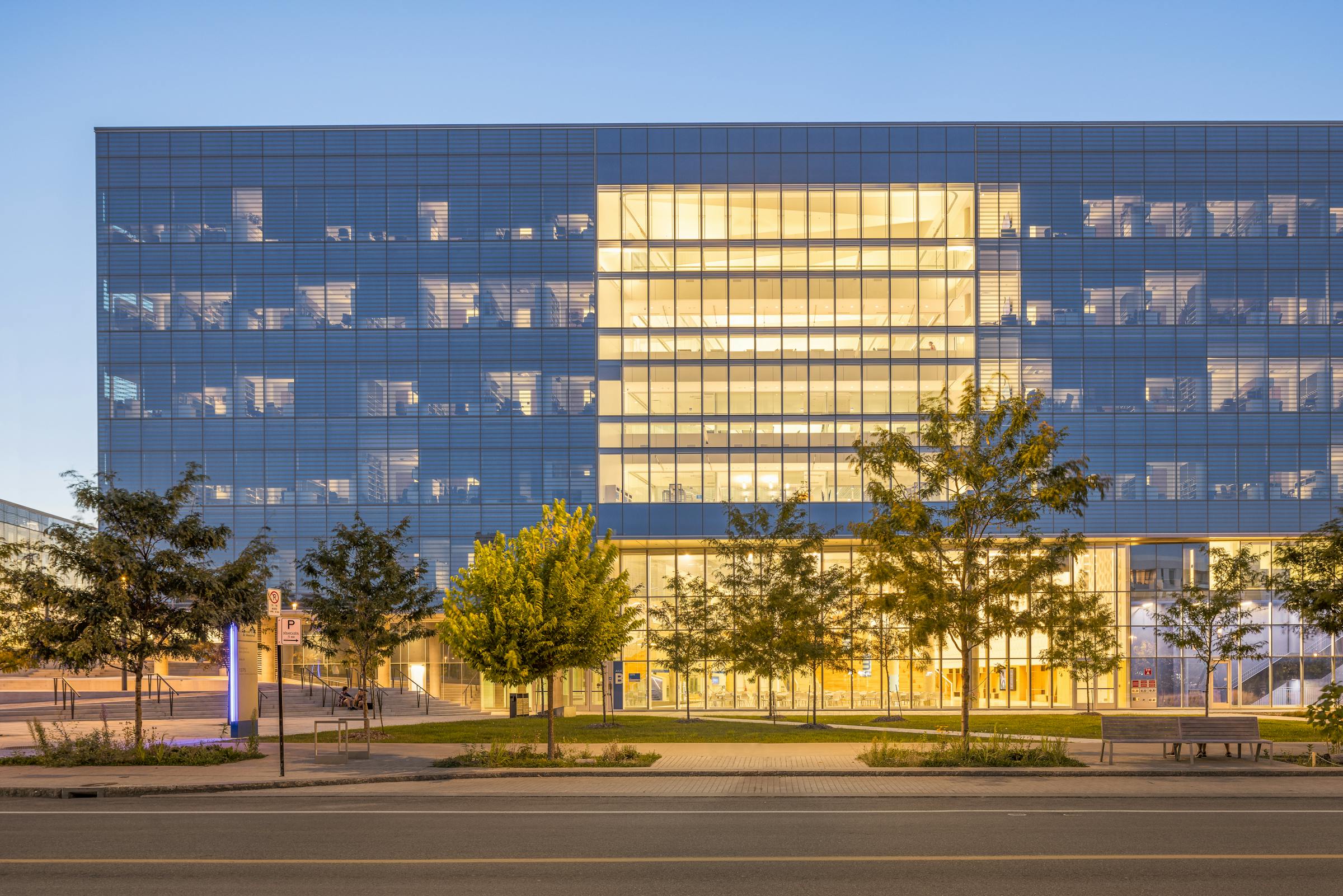 A frontal perspective of a glass institutional building, illuminated primarily by artificial light, revealing the interior.
