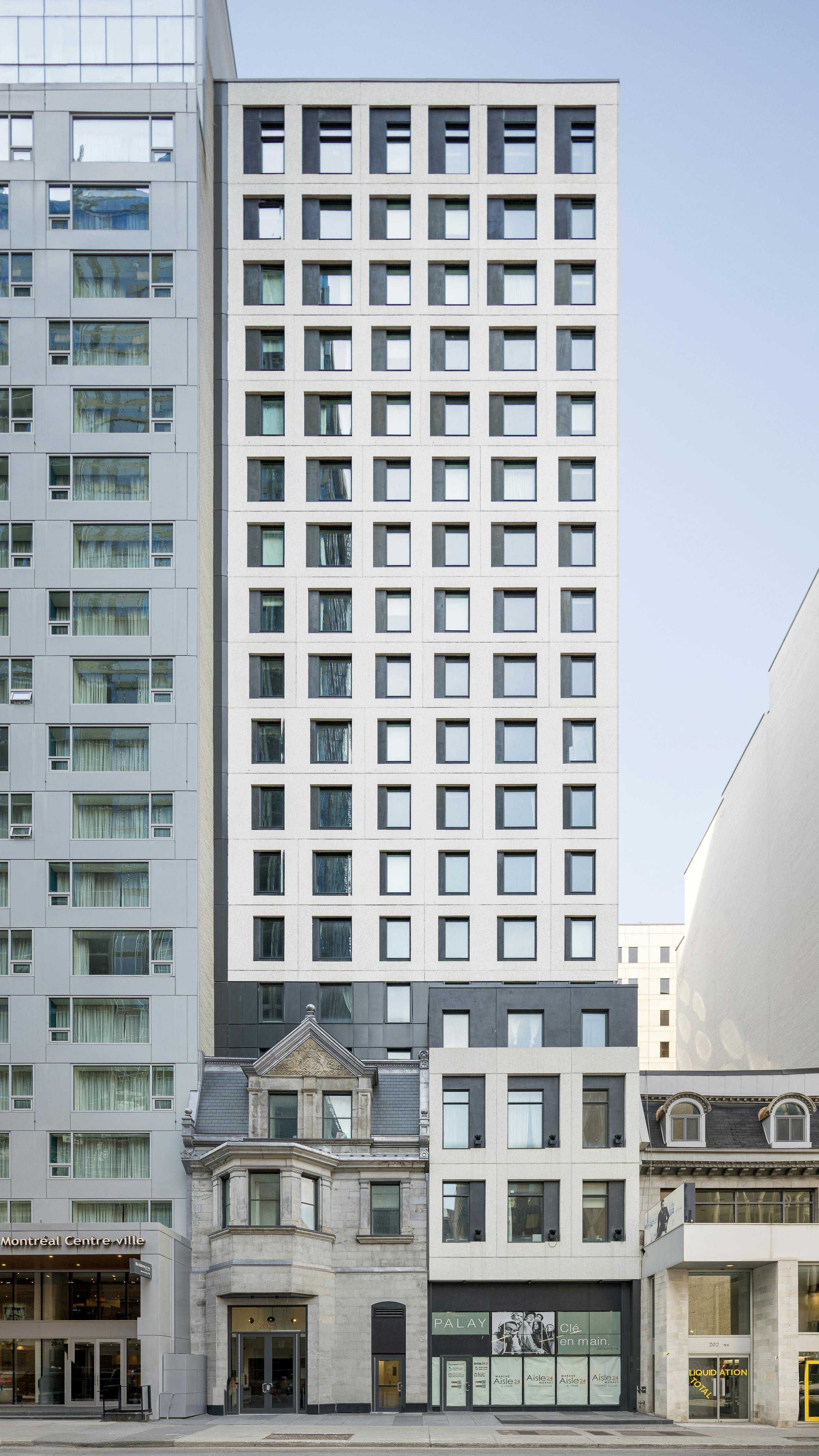 Élévation frontale d’un immeuble à trame régulière de fenêtres carrées, juxtaposé à une ancienne maison de pierre