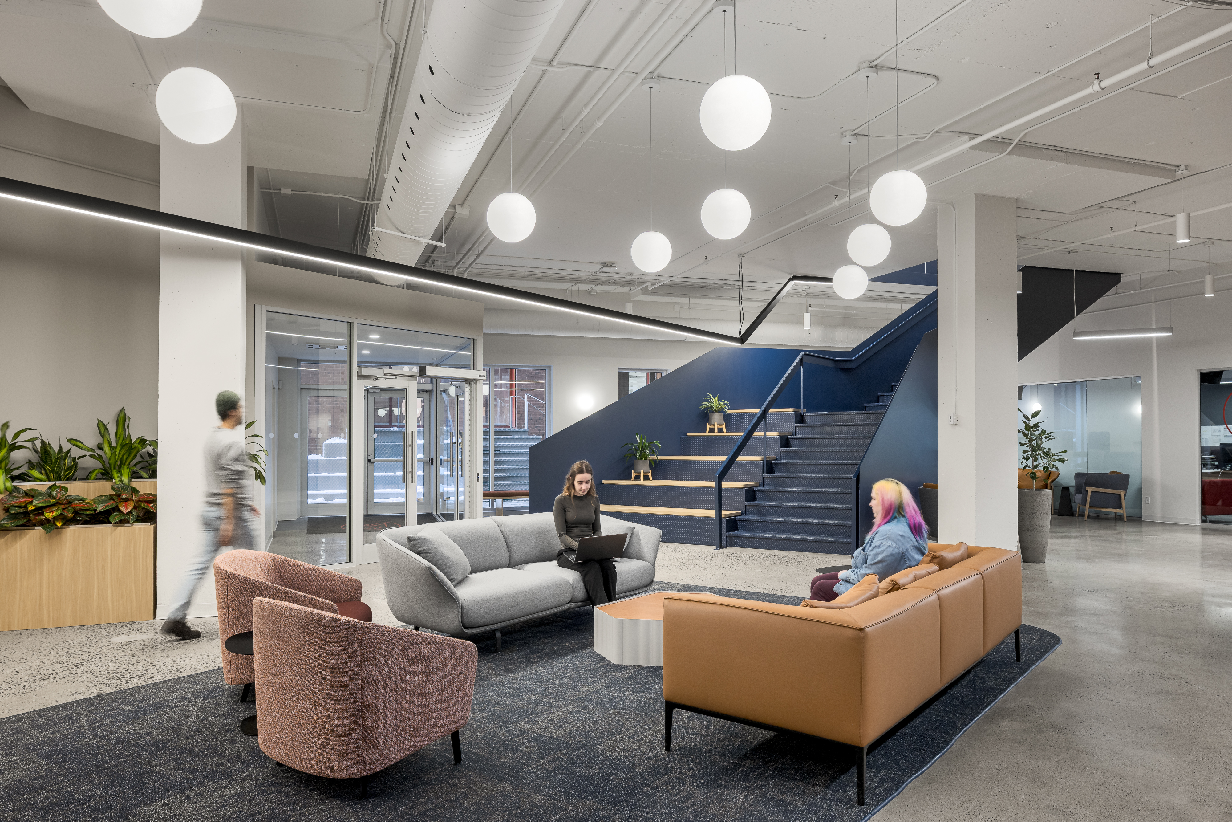 Photographie d’un espace de détente en milieu de travail avec fauteuils design et escalier architectural bleu.