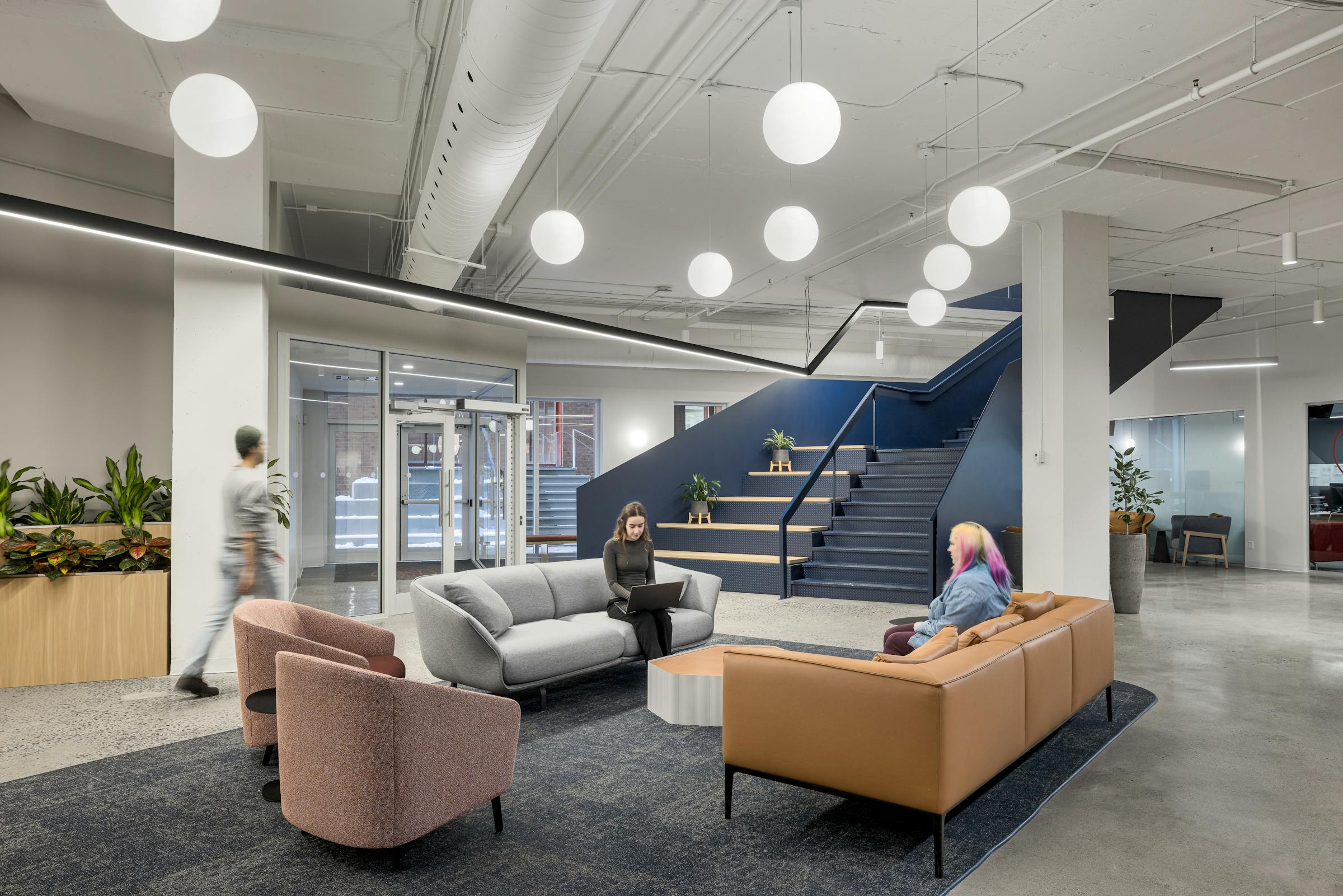 Photographie d’un espace de détente en milieu de travail avec fauteuils design et escalier architectural bleu.
