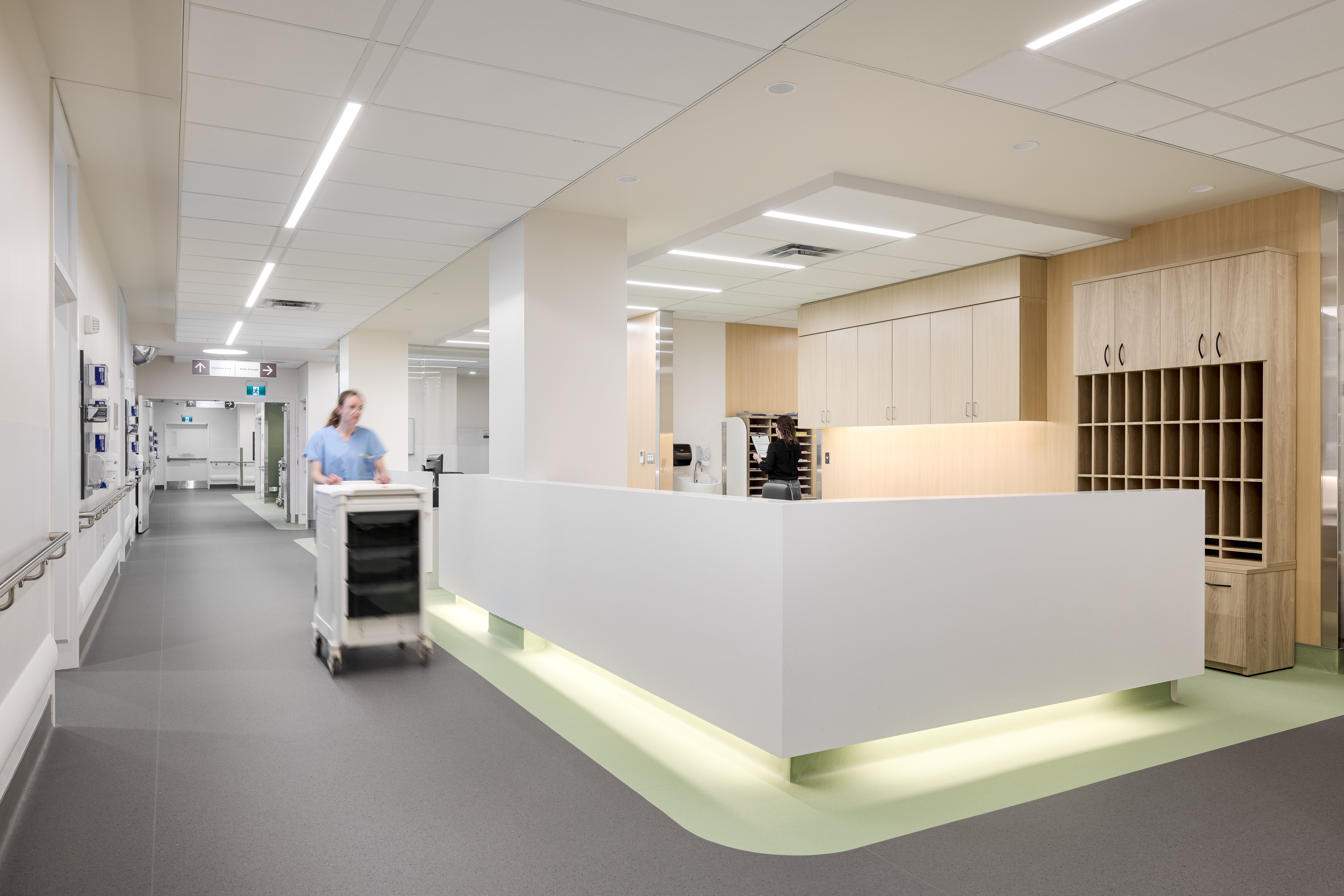 Photographie d’architecture d’un corridor d’hôpital lumineux avec fresque murale et personnel soignant en mouvement.