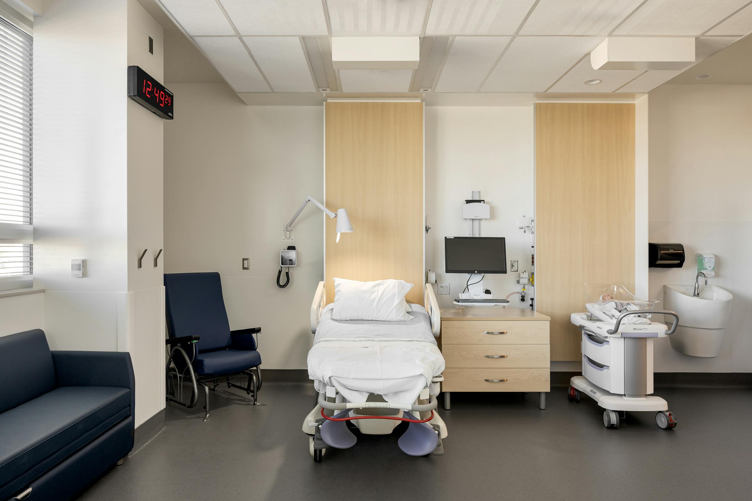 Chambre d’hôpital minimaliste avec lit médicalisé et mobilier intégré, photographie architecturale contemporaine.