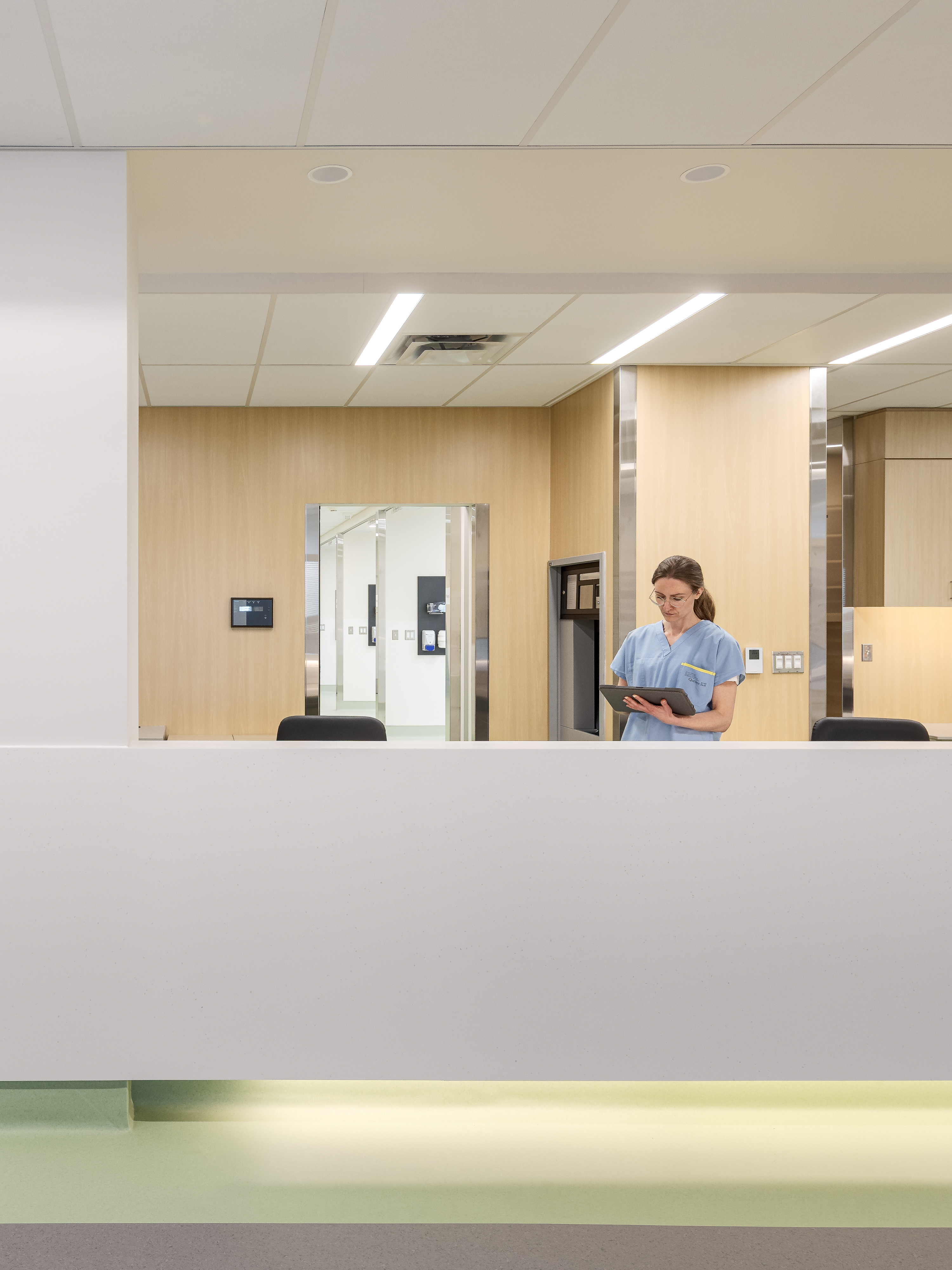 Station infirmière en hôpital avec habillage de bois et éclairage indirect, photographiée en grand angle.