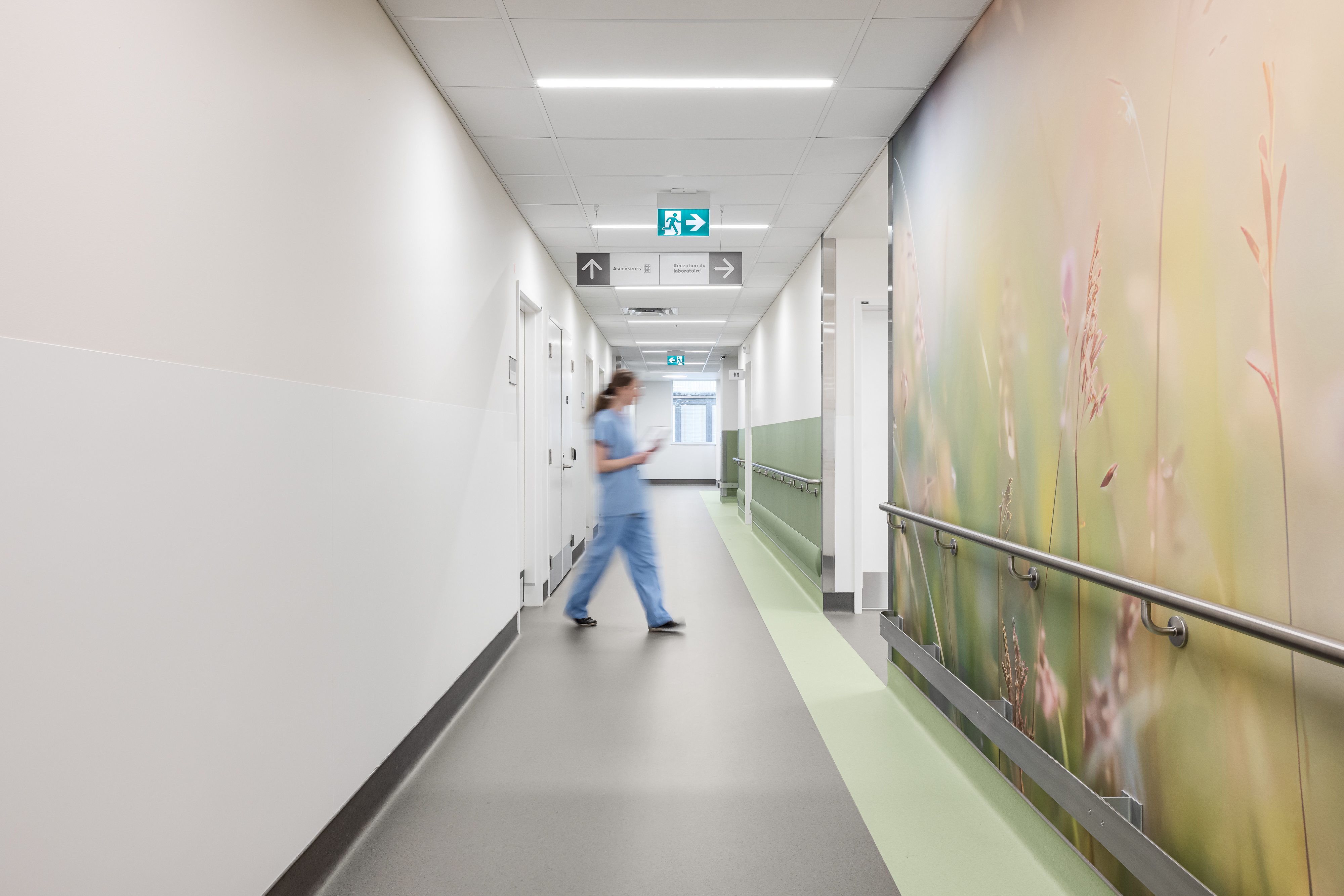 Photographie de clinique hospitalière montrant un long couloir épuré avec signalétique et main courante intégrée à l’architecture.