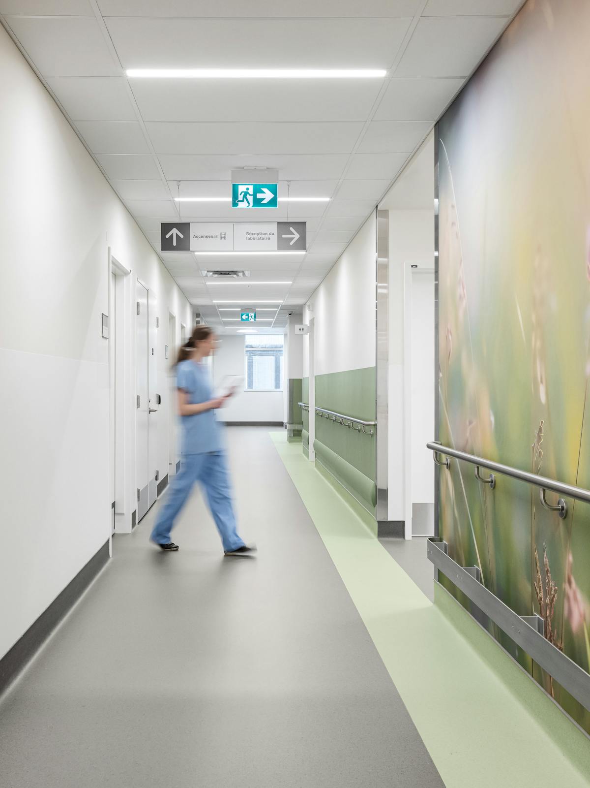 Photographie de clinique hospitalière montrant un long couloir épuré avec signalétique et main courante intégrée à l’architecture.