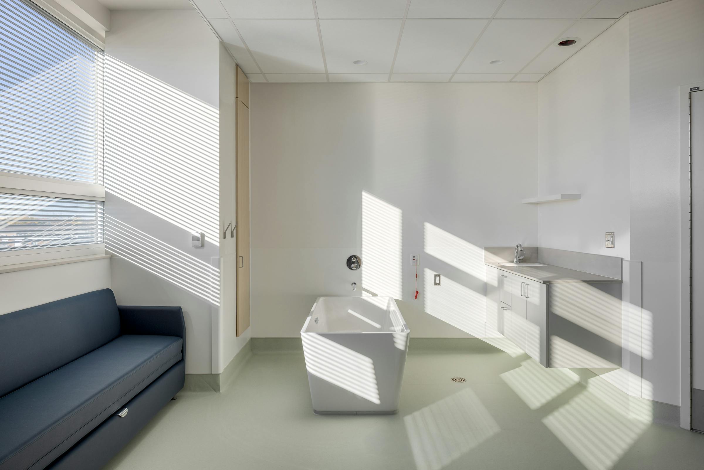 Chambre de clinique hospitalière moderne avec équipement médical et lumière naturelle, en photographie d’architecture.
