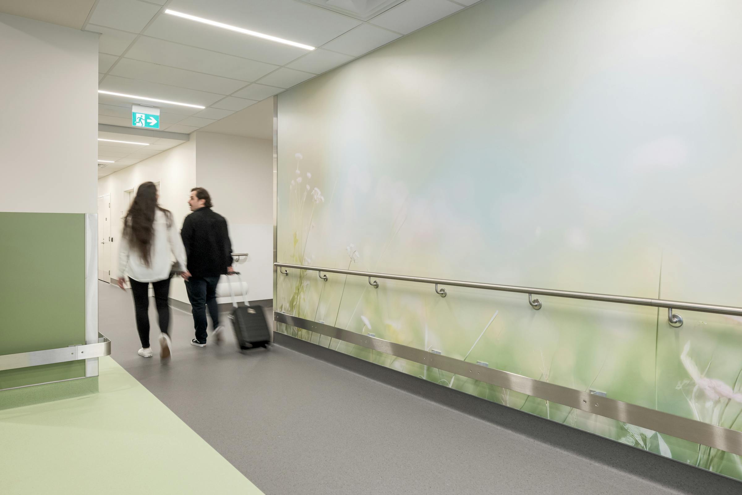 Corridor de clinique aux tons vert pâle et mur illustré, documenté en photographie d’architecture.