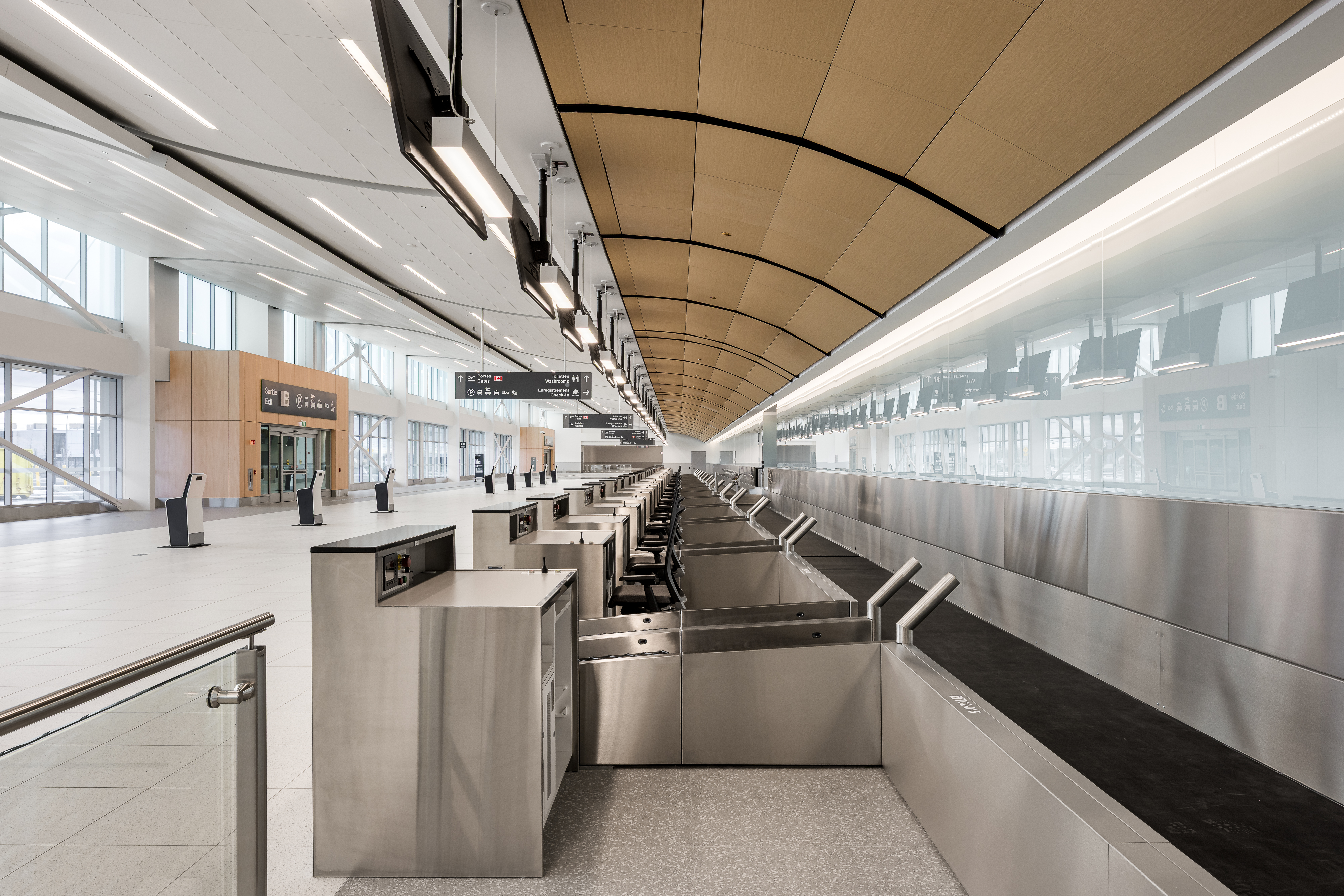 Grand hall d’enregistrement lumineux avec plafond en lattes de bois et comptoirs d’enregistrement alignés.