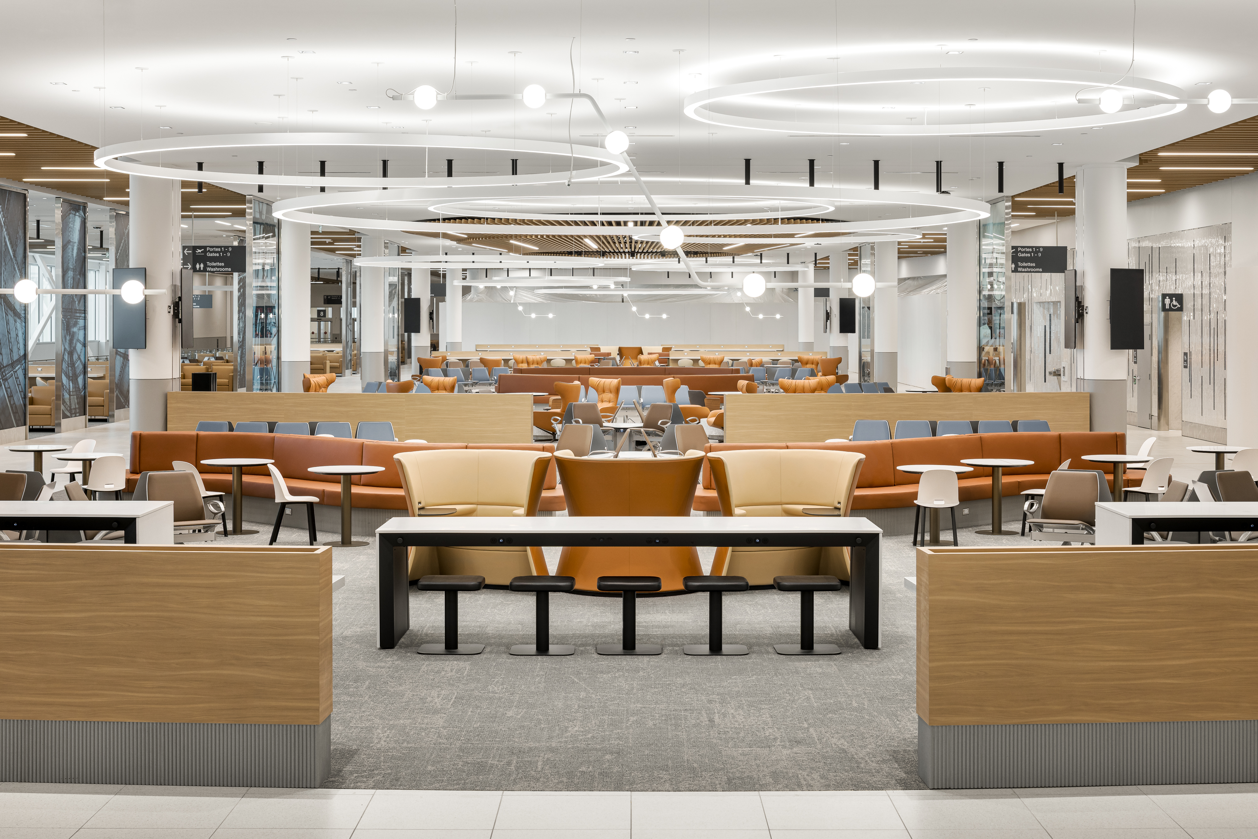 Photographie d’architecture intérieure du lounge de l’aéroport métropolitain de Montréal avec plafond circulaire lumineux et mobilier contemporain.