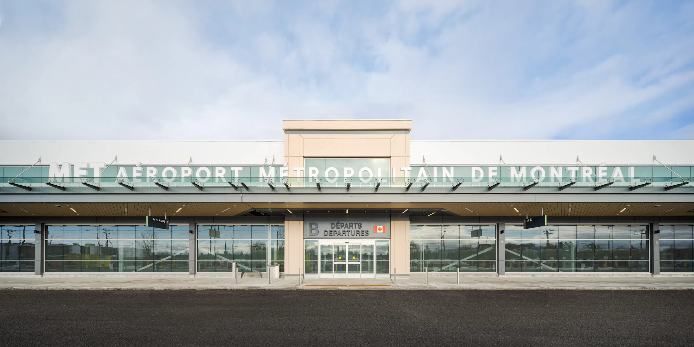 Façade moderne de l’aéroport métropolitain de Montréal photographiée de face, avec une architecture minimaliste et une entrée principale vitrée.