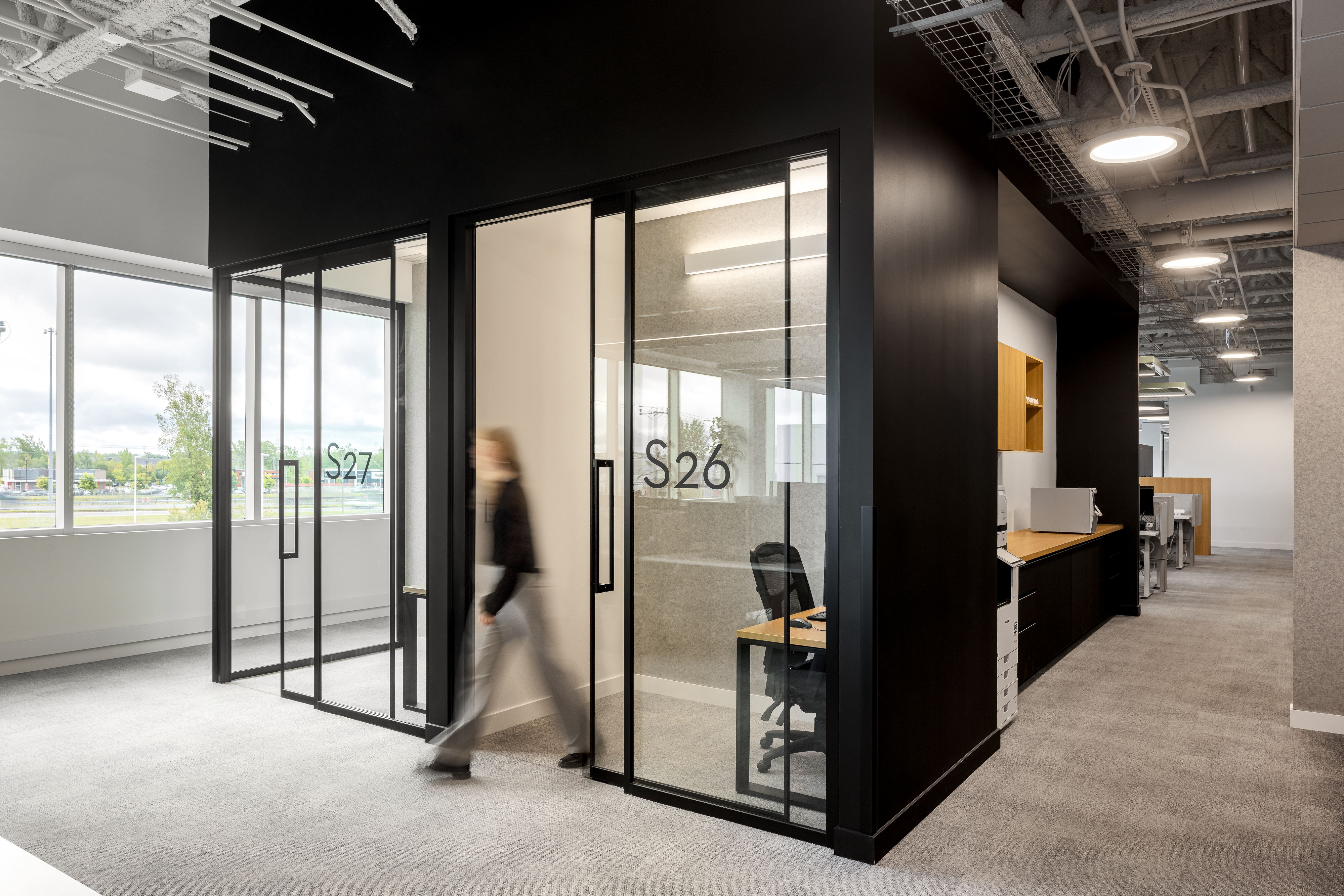 Photographie d’architecture d’un bureau vitré avec salles de réunion et circulation intérieure dans un espace de travail contemporain.