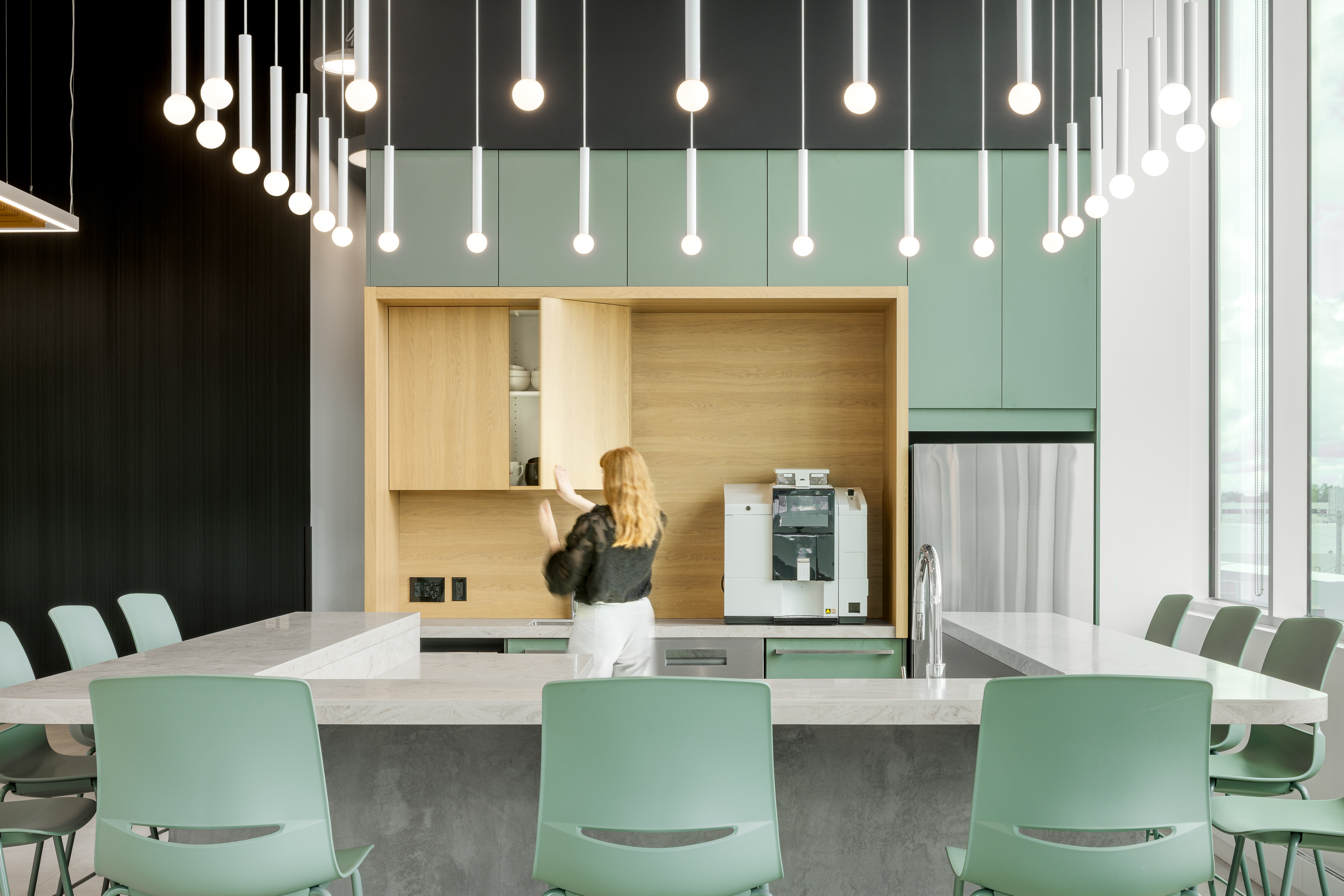 Photographie d’architecture d’une cafétéria d’entreprise avec cuisine intégrée, luminaires suspendus et design intérieur contemporain.