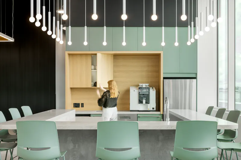 Photographie d’architecture d’une cafétéria d’entreprise avec cuisine intégrée, luminaires suspendus et design intérieur contemporain.