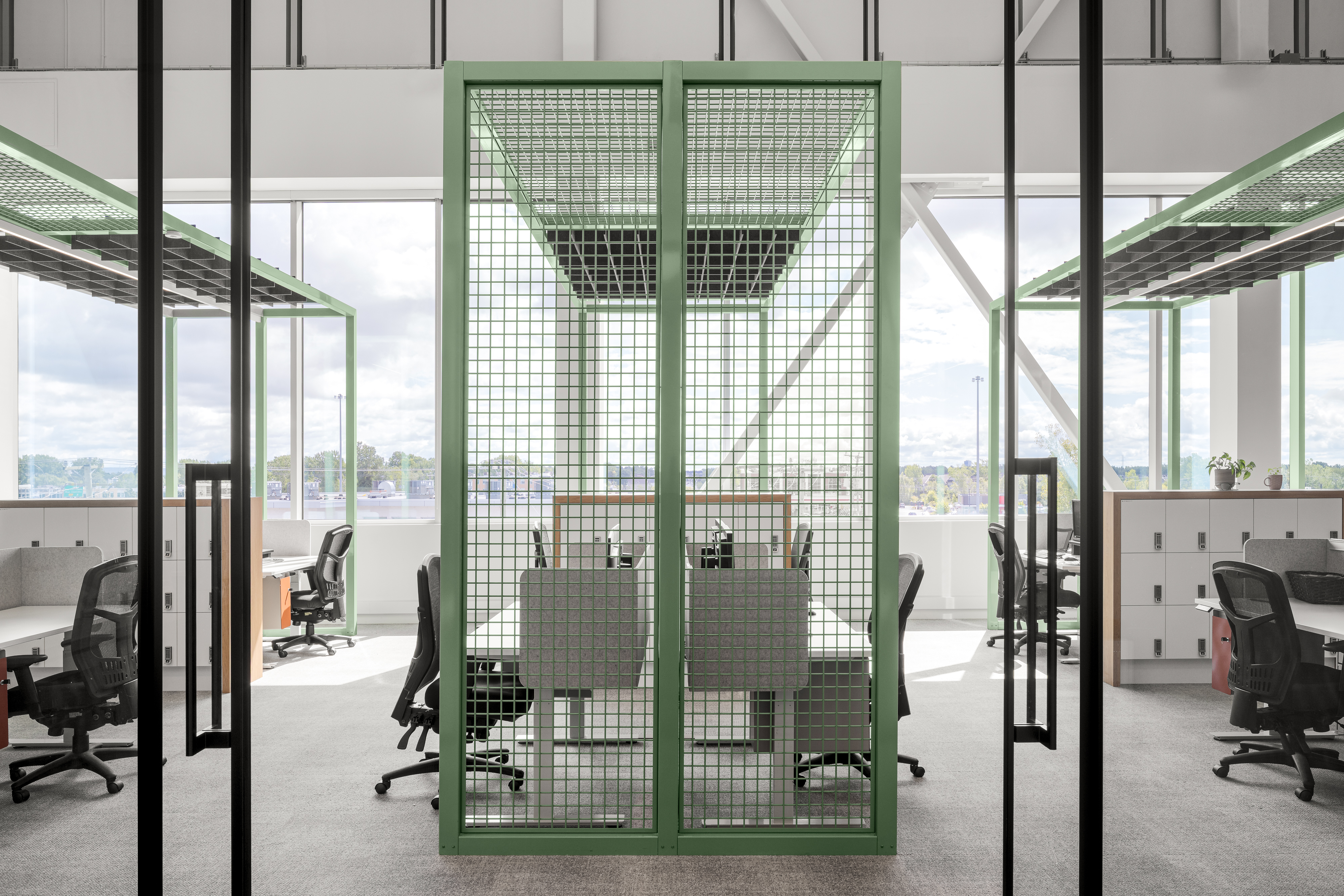 Photographie d’architecture d’un espace de travail collaboratif avec structure métallique verte et design de bureaux contemporains.