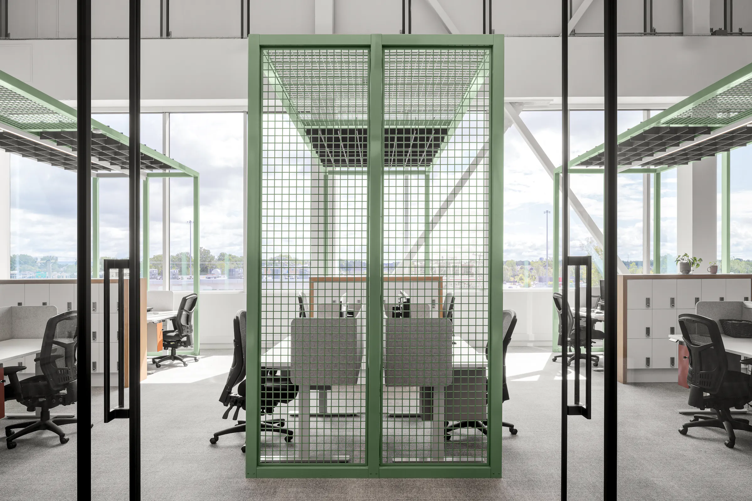 Photographie d’architecture d’un espace de travail collaboratif avec structure métallique verte et design de bureaux contemporains.