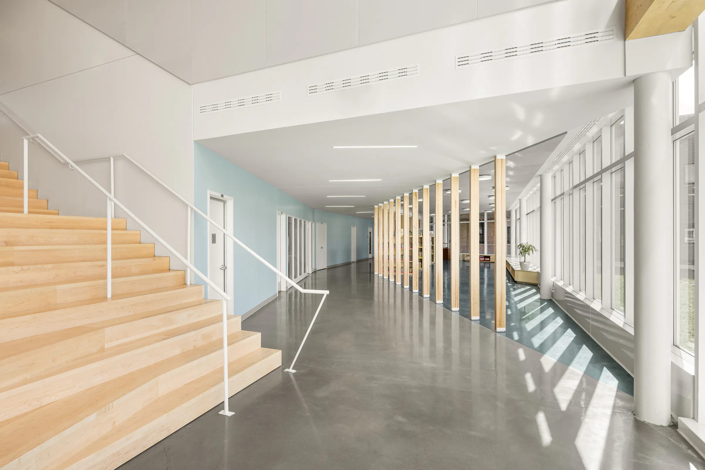 Photographie d’architecture d’un espace de circulation dans une école moderne avec escalier en bois et design intérieur minimaliste.
