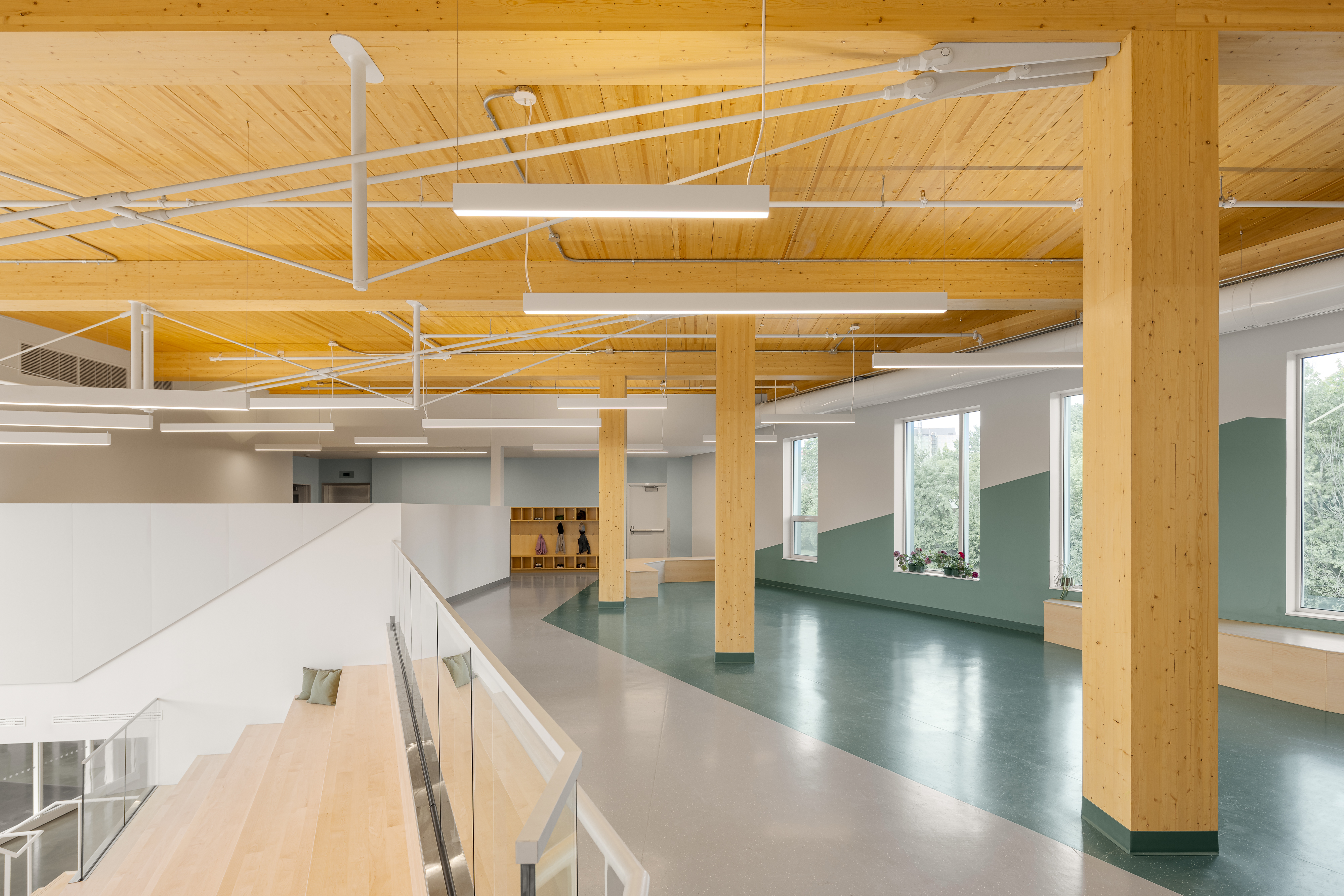 Photographie d’architecture d’un espace multifonctionnel d’école avec colonnes en bois, lumière naturelle et design intérieur moderne.