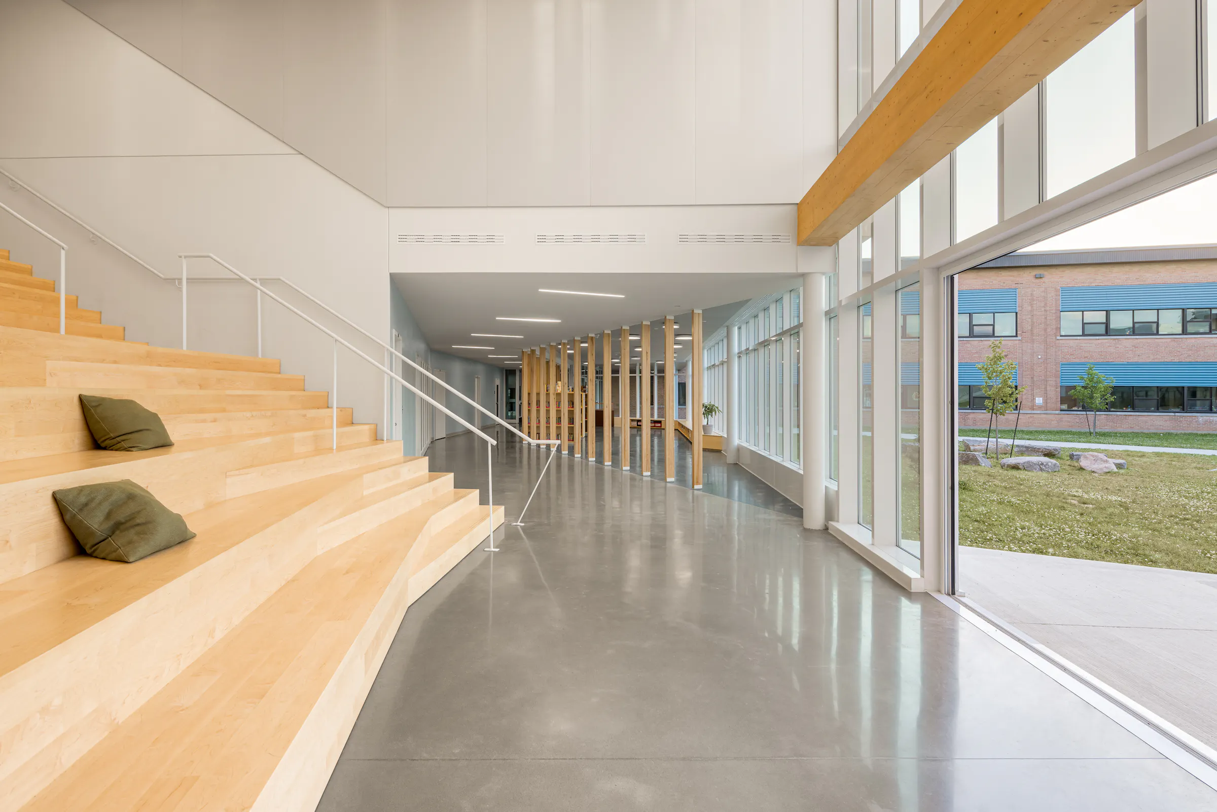 Photographie d’architecture d’un grand espace intérieur scolaire avec gradins en bois et façade vitrée sur la cour.