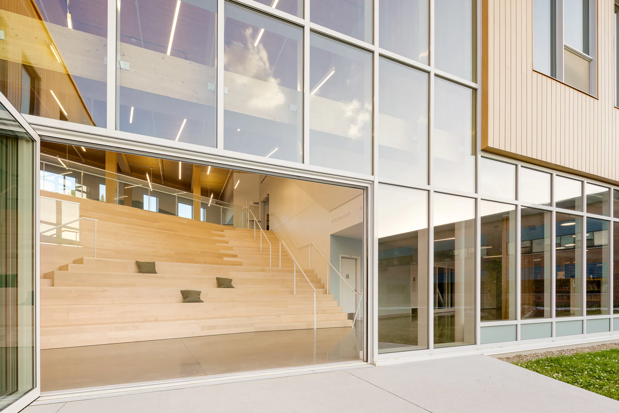 Photographie d’architecture d’un gradin en bois dans une école contemporaine avec grandes fenêtres et lumière naturelle.