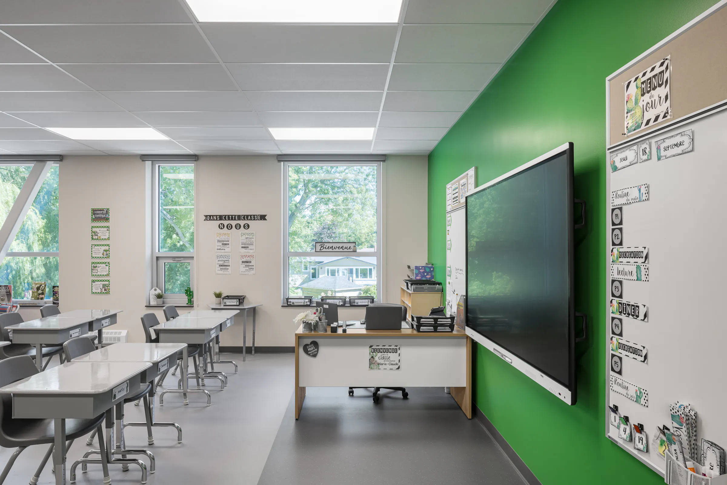 Local de classe lumineux de l'École des Saules, L'Assomption. Mur vert et grandes fenêtres sur le site boisé. Photo : Studio Tarmac.